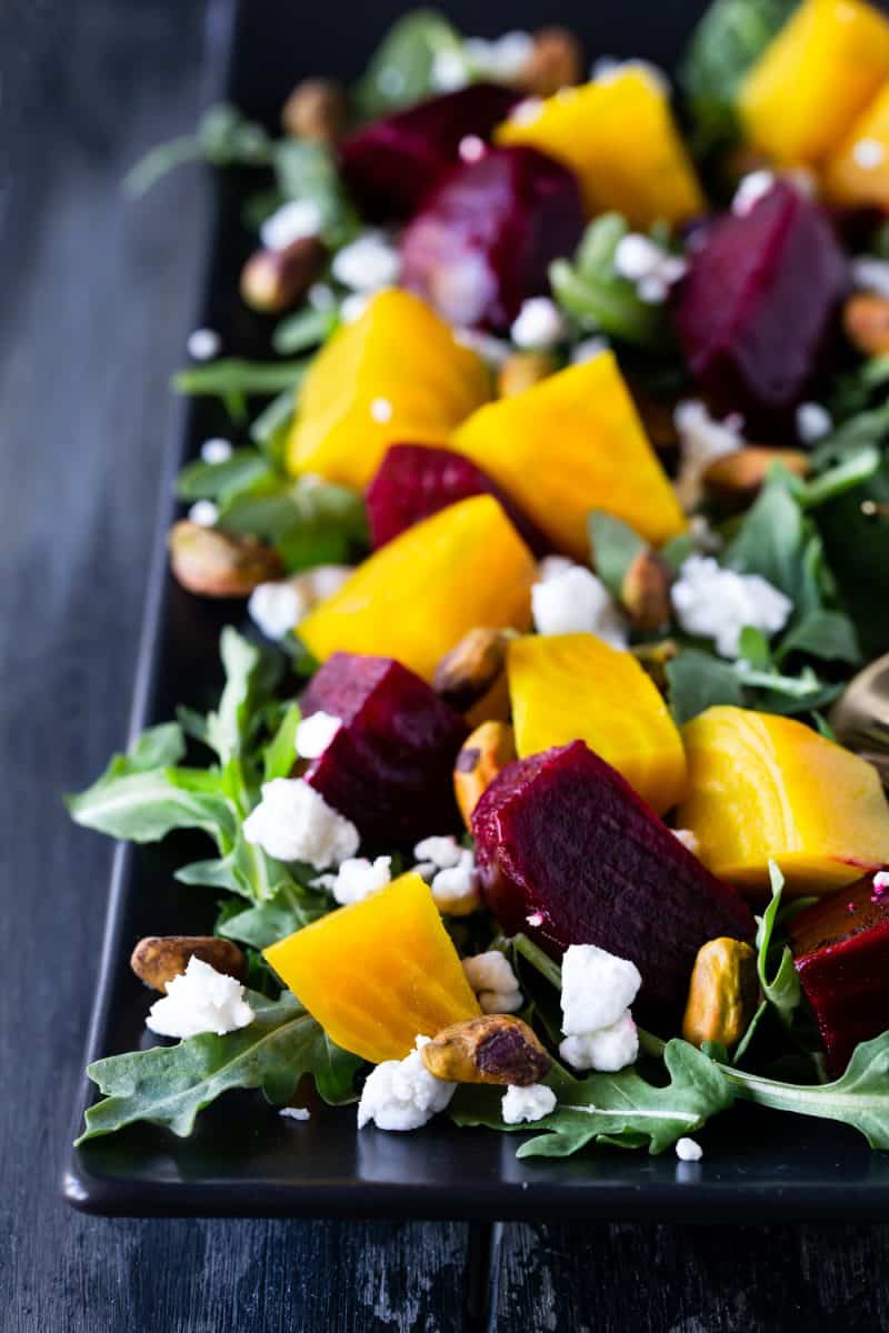 Close up of Roasted Beet Salad with Goat Cheese, Arugula and Pistachios on a black platter.