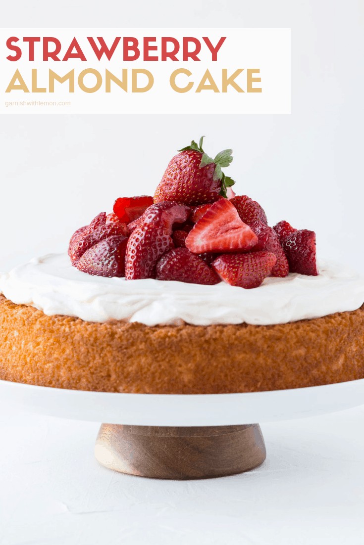 Almond cake on a cake stand with whipped topping and fresh strawberries.