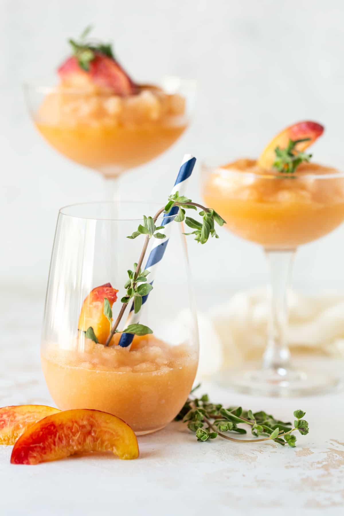 Three glasses of Peach Frosé. Garnished with fresh peach slices and fresh marjoram. 