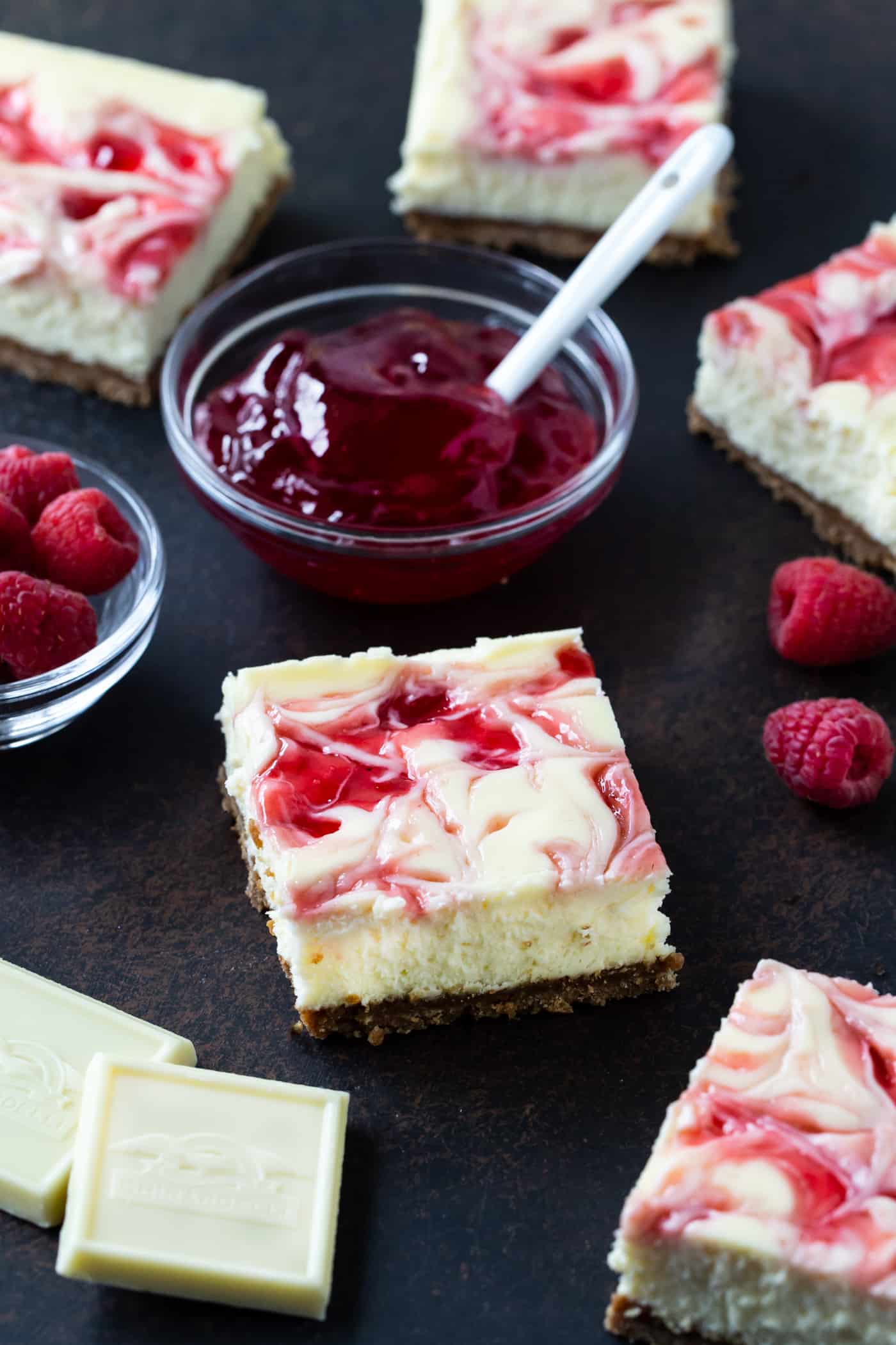 Cut Raspberry White Chocolate Cheesecake bars on a black serving tray with fresh berries for garnish.