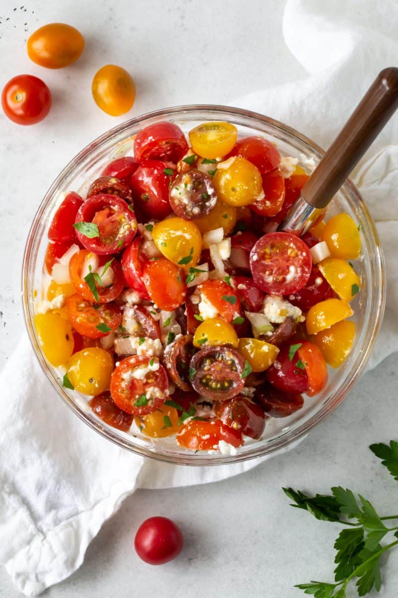 Large glass bowl filled with Tomato Feta Salad with Sweet Onion, with chopped parsley.