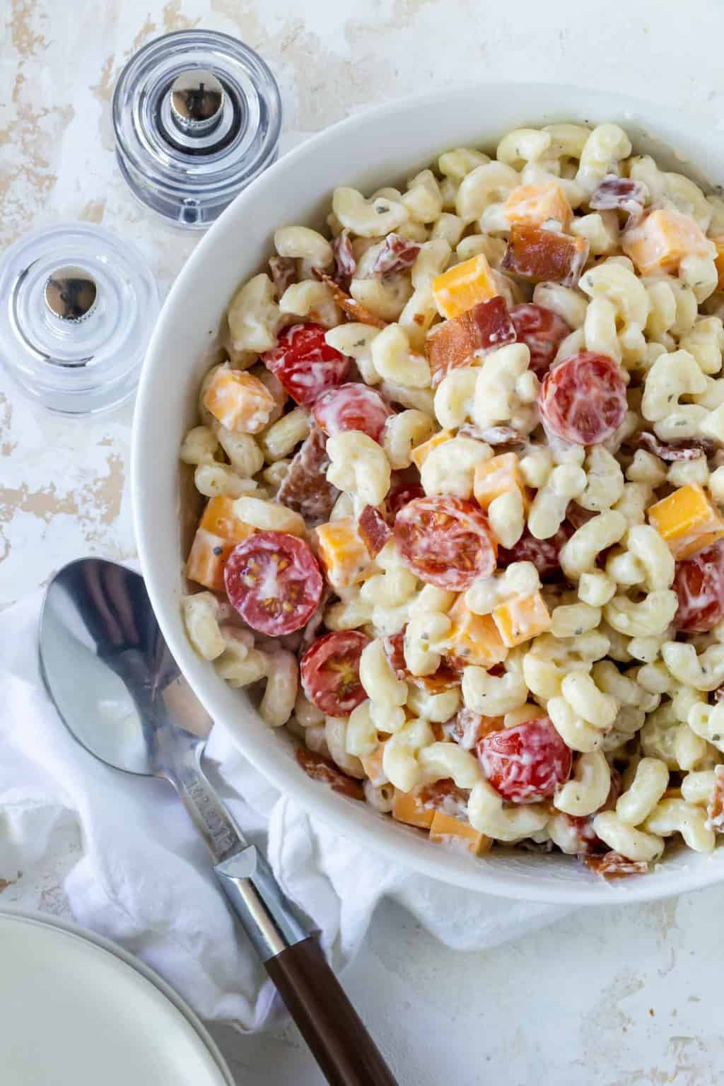 bacon ranch pasta salad in a white bowl on a white surface with a spoon for serving.