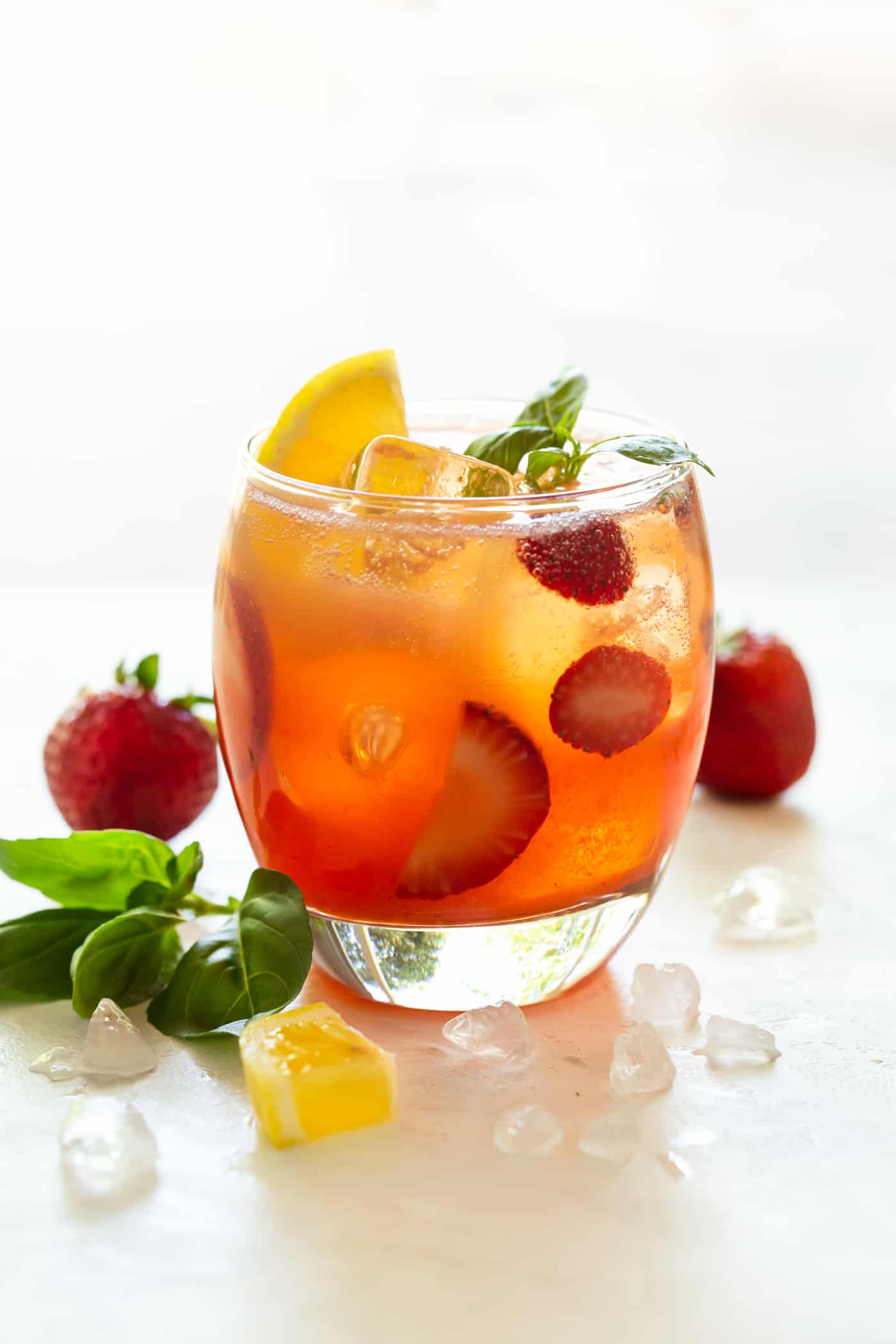 A single cocktail in a low ball glass . Garnished with fresh strawberries and basil.