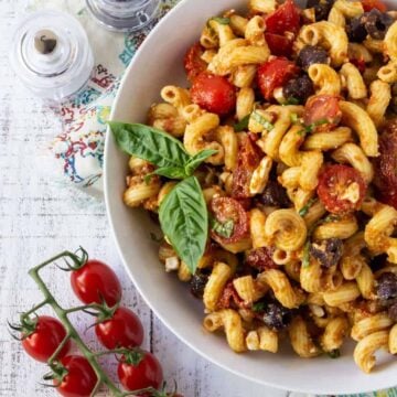 Pasta Salad in a white bowl with cherry tomatoes and fresh basil.