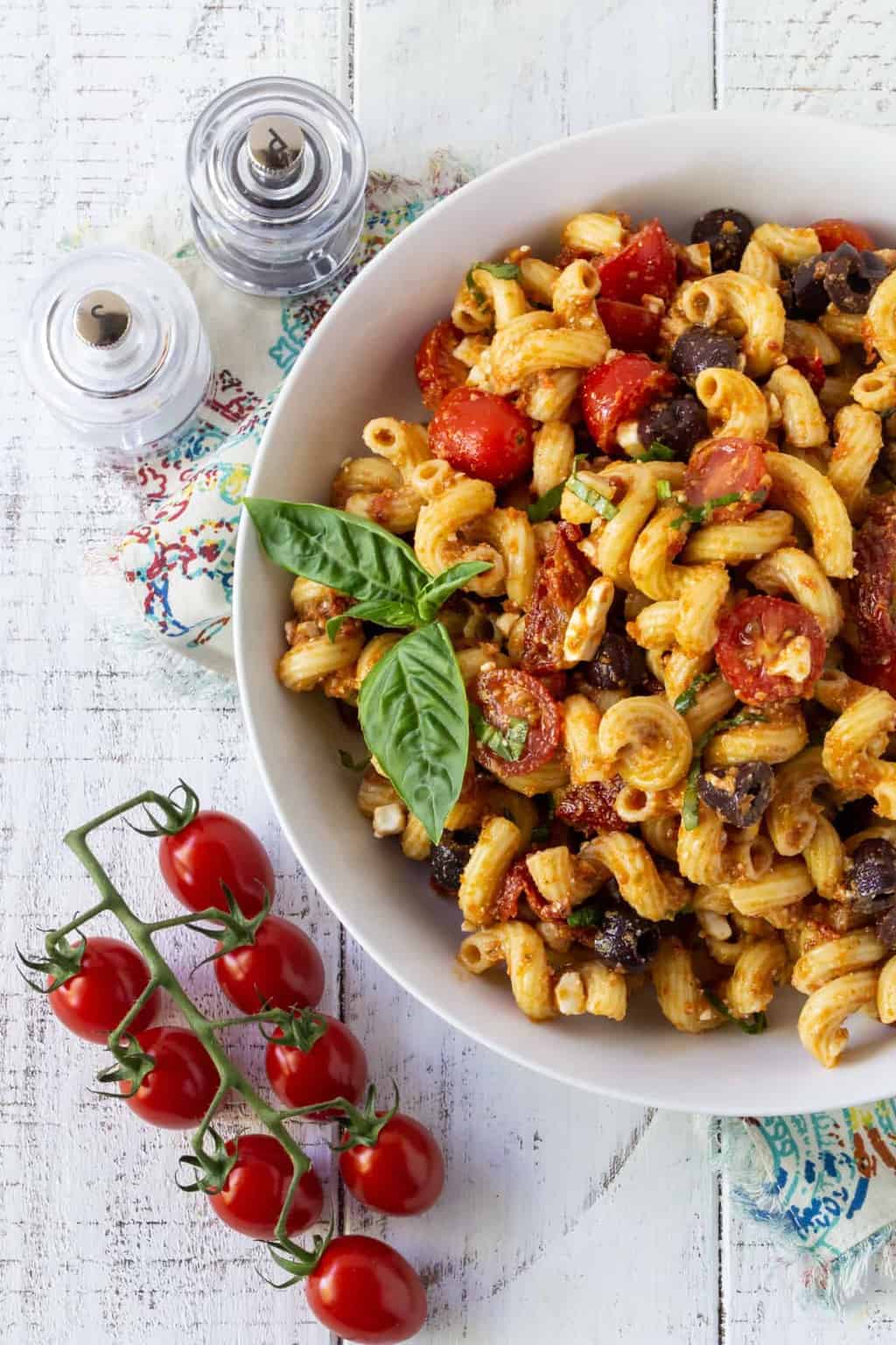 Pasta Salad in a white bowl with cherry tomatoes and fresh basil.