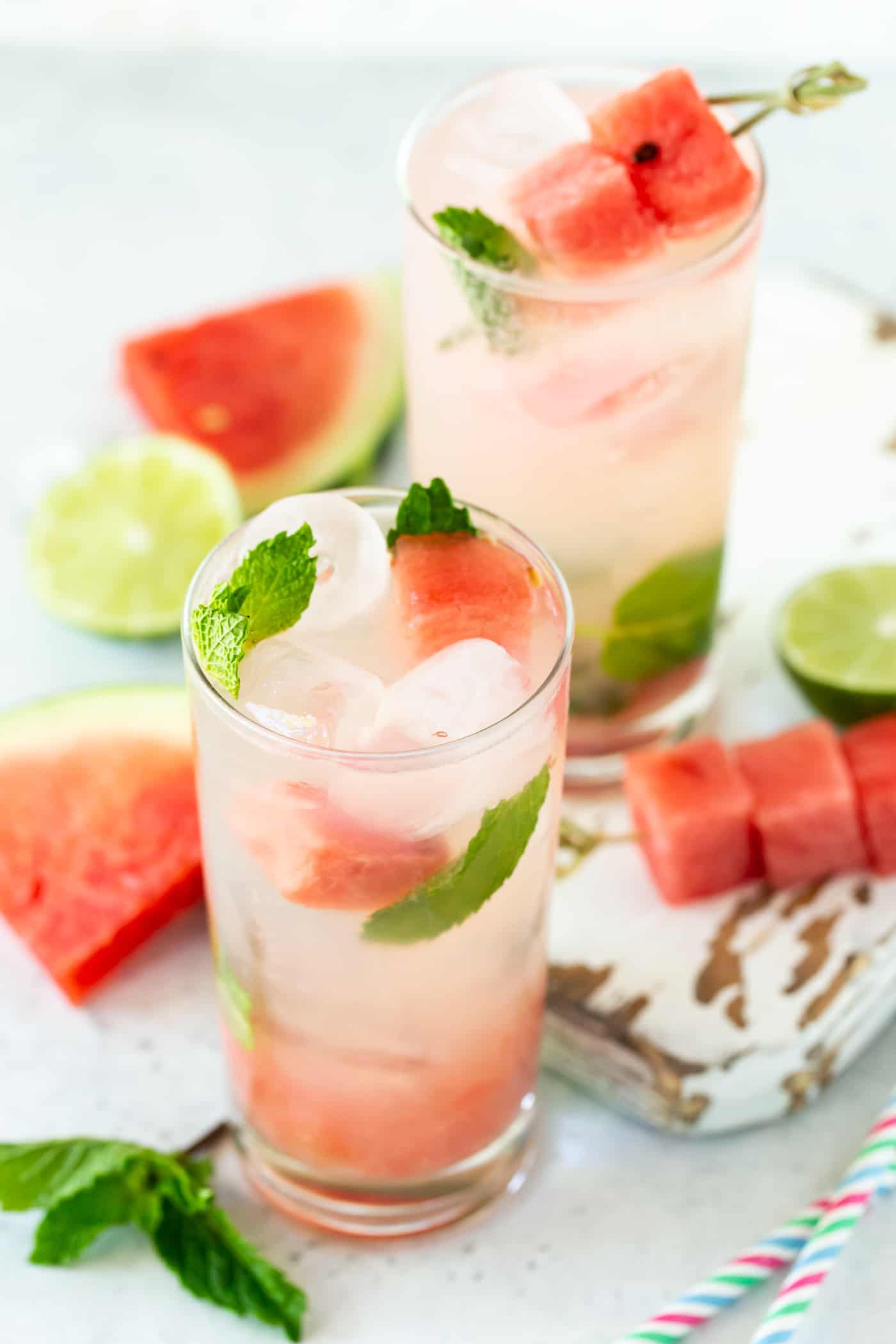 Two ice-filled highball glasses filled with Watermelon Mojitos. Garnished with fresh watermelon cubes and mint leaves. 