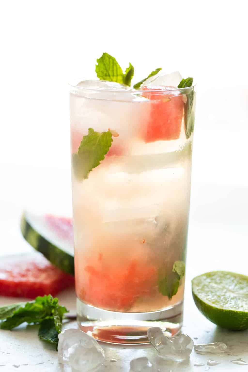 A single highball glass filled with ice and a watermelon mojito cocktail. Garnished with fresh watermelon and mint leaves. 