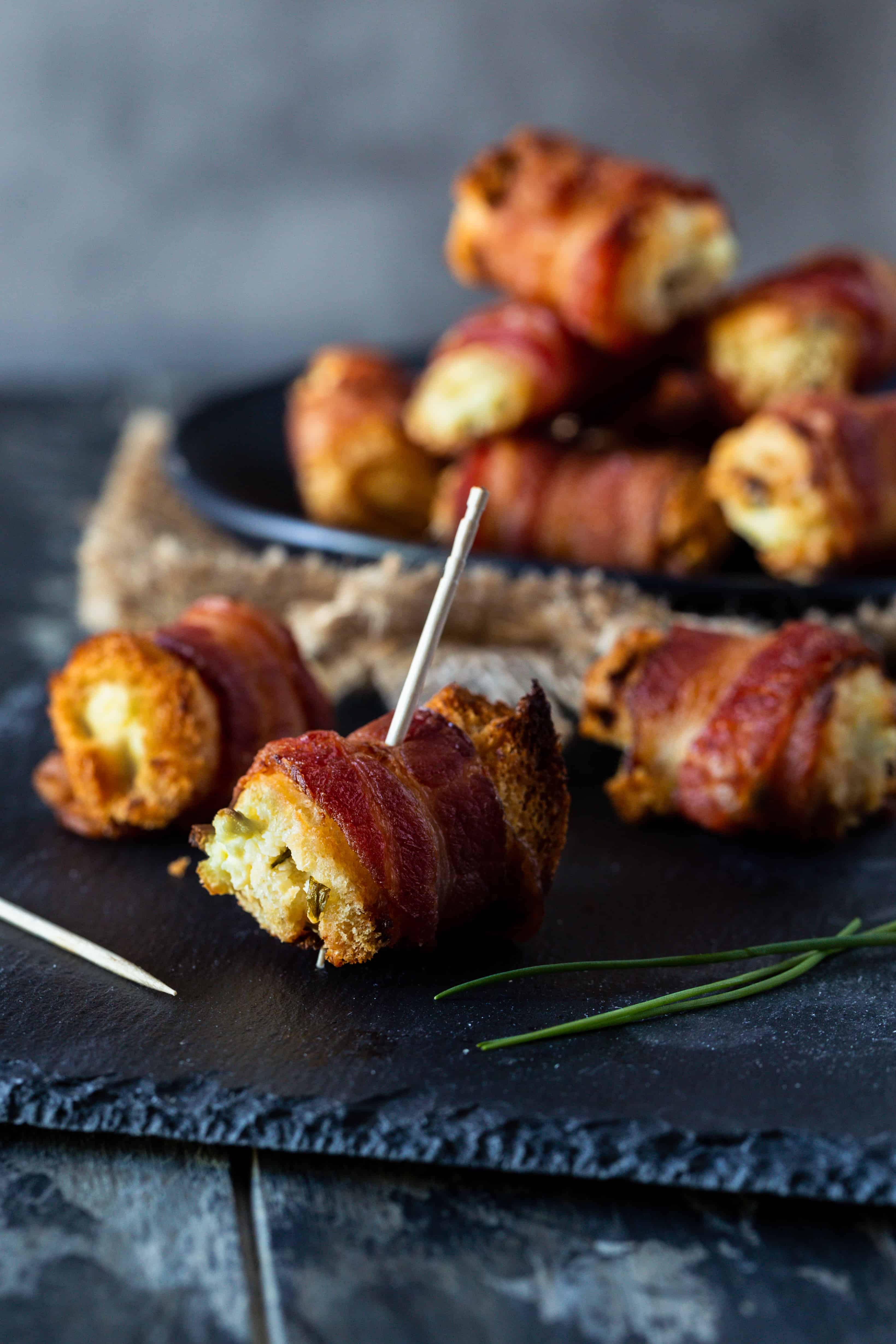 Close up image of bacon cream cheese bites on a black plate with a toothpick for eating.