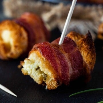 Bacon cream cheese bites on a black surface with toothpicks for serving and fresh chives for garnish.