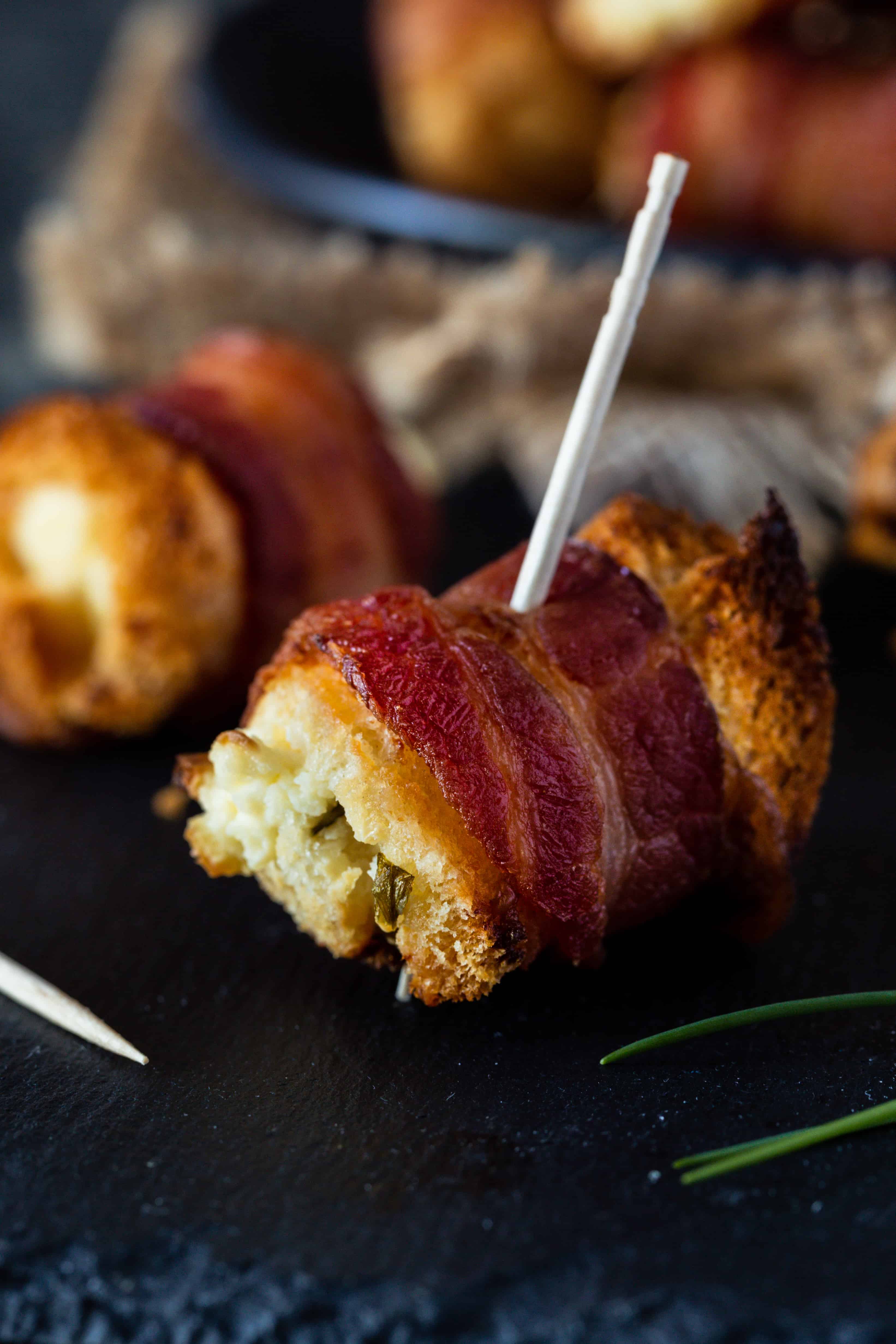 Bacon cream cheese bites on a black surface with toothpicks for serving and fresh chives for garnish.