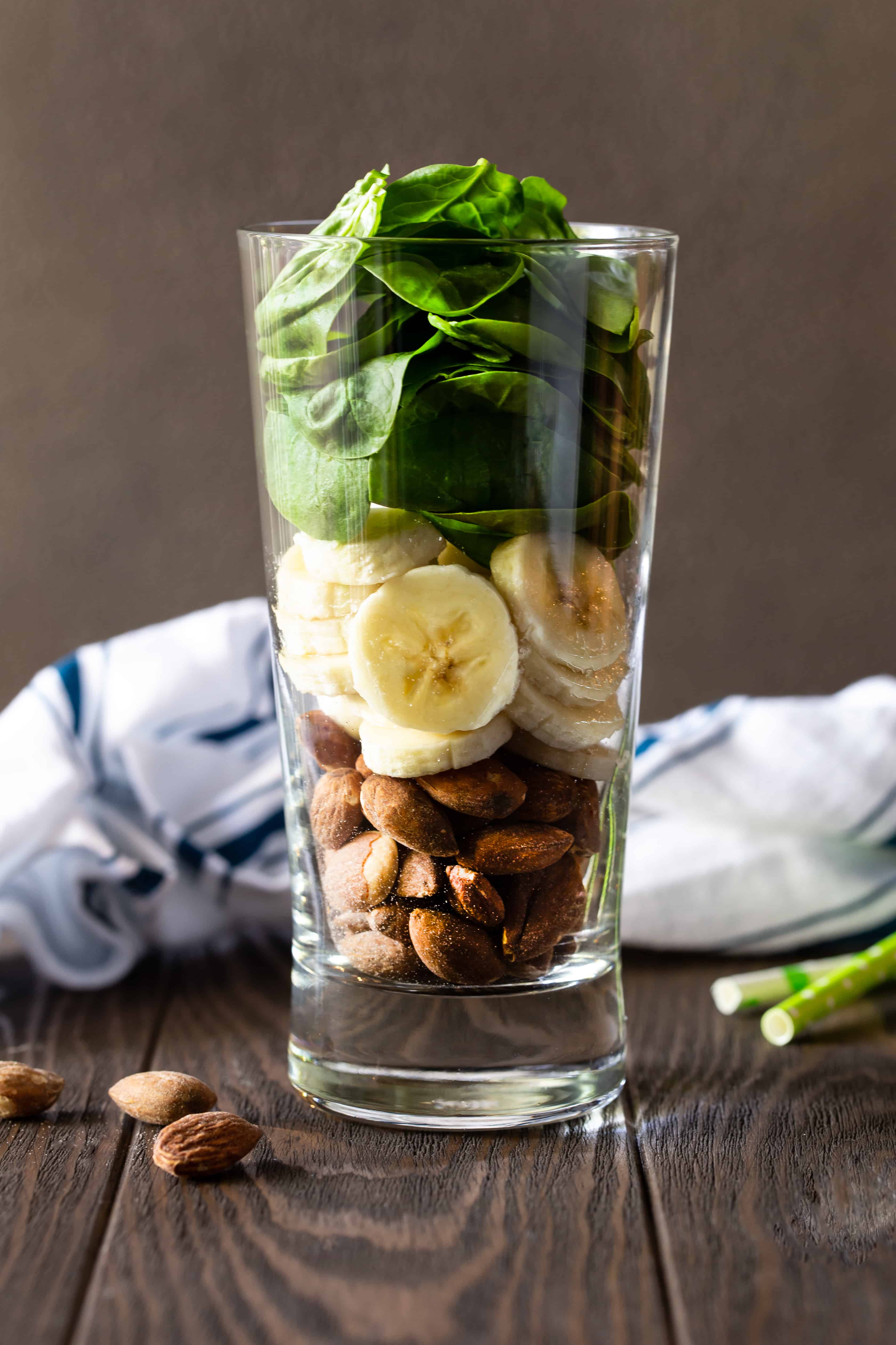 Glass filled with smoothie ingredients including fresh spinach, banana slices and almonds.