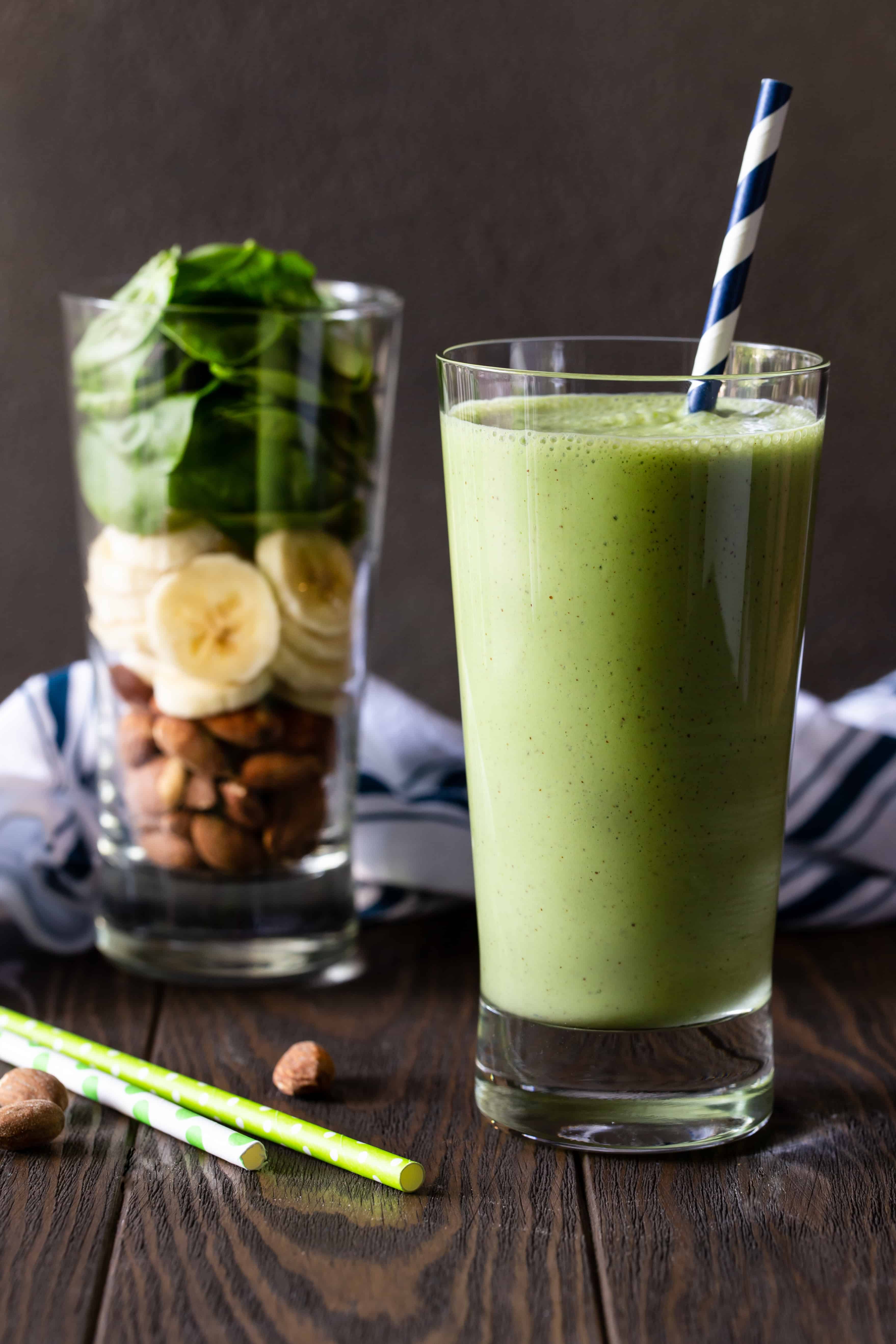 Two glasses on a wood board. One is filled with raw ingredients for smoothie and other is filled with blended Smoothie.