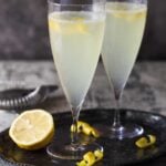 Tall champagne flutes filled with cocktails with lemon slices for garnish.