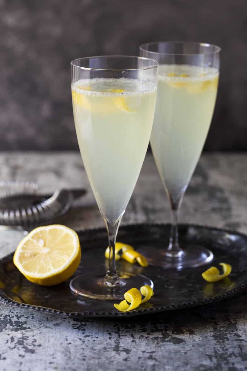 Tall champagne flutes filled with cocktails with lemon slices for garnish.