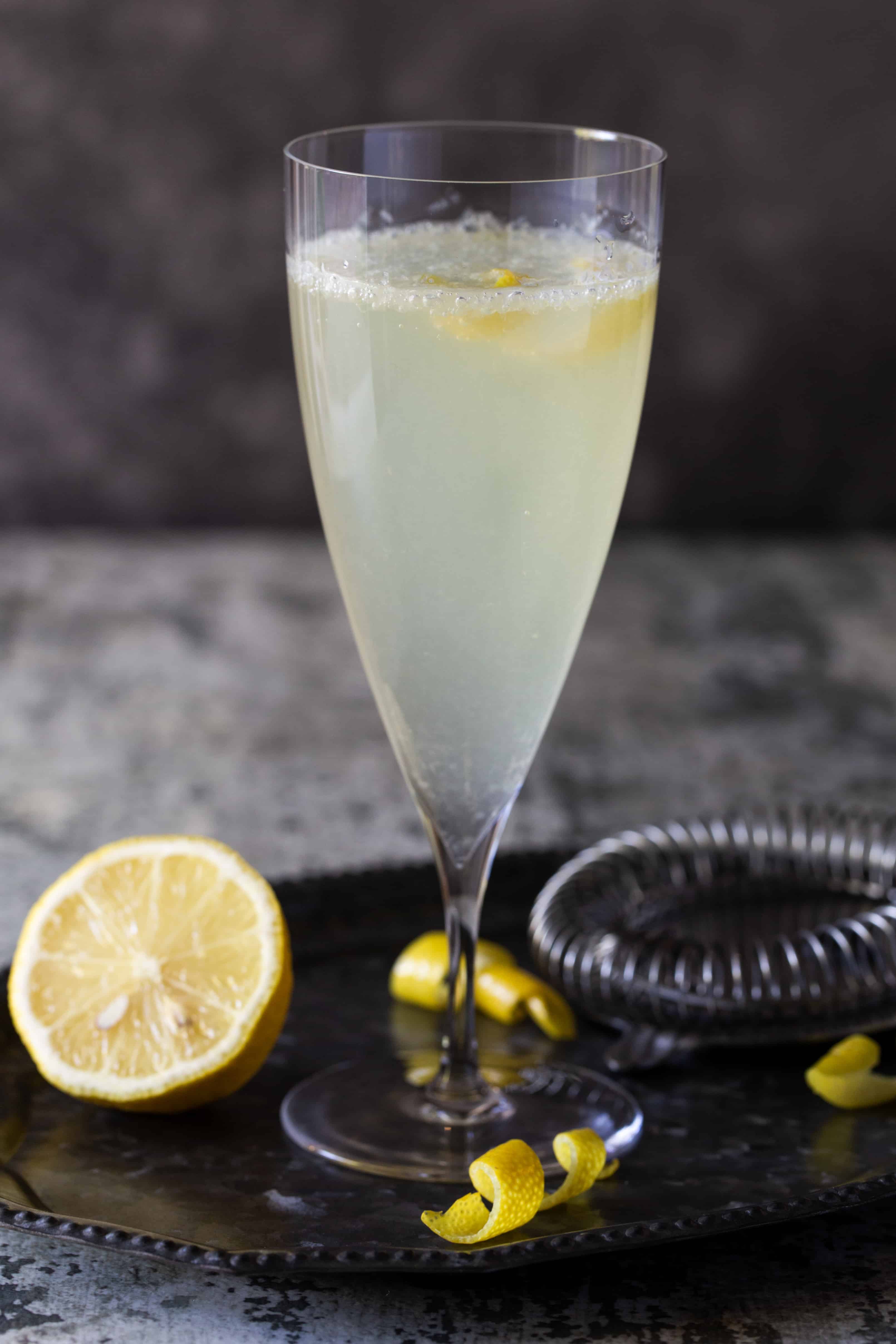 Single cocktail in a tall flute garnished with a lemon slice on a dark background.