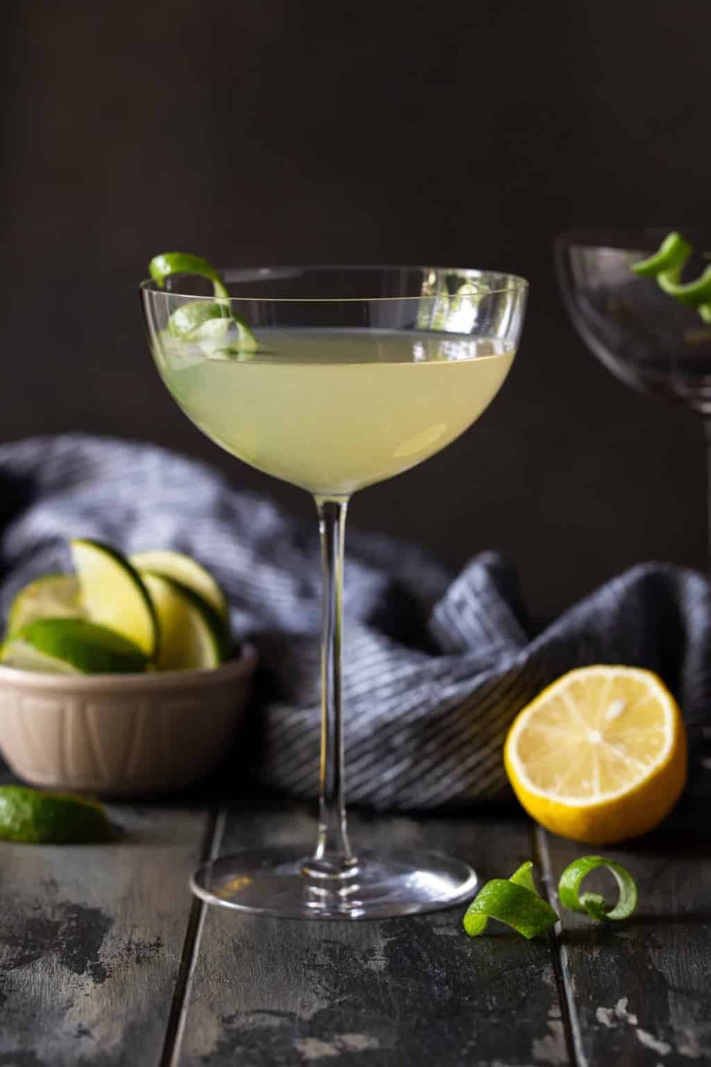 martini in tall coupe glass on a dark background ,with half of a lemon and lime on plate.