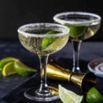 Cocktails in coupe glasses with sugar rims and a lime wedge for garnish.