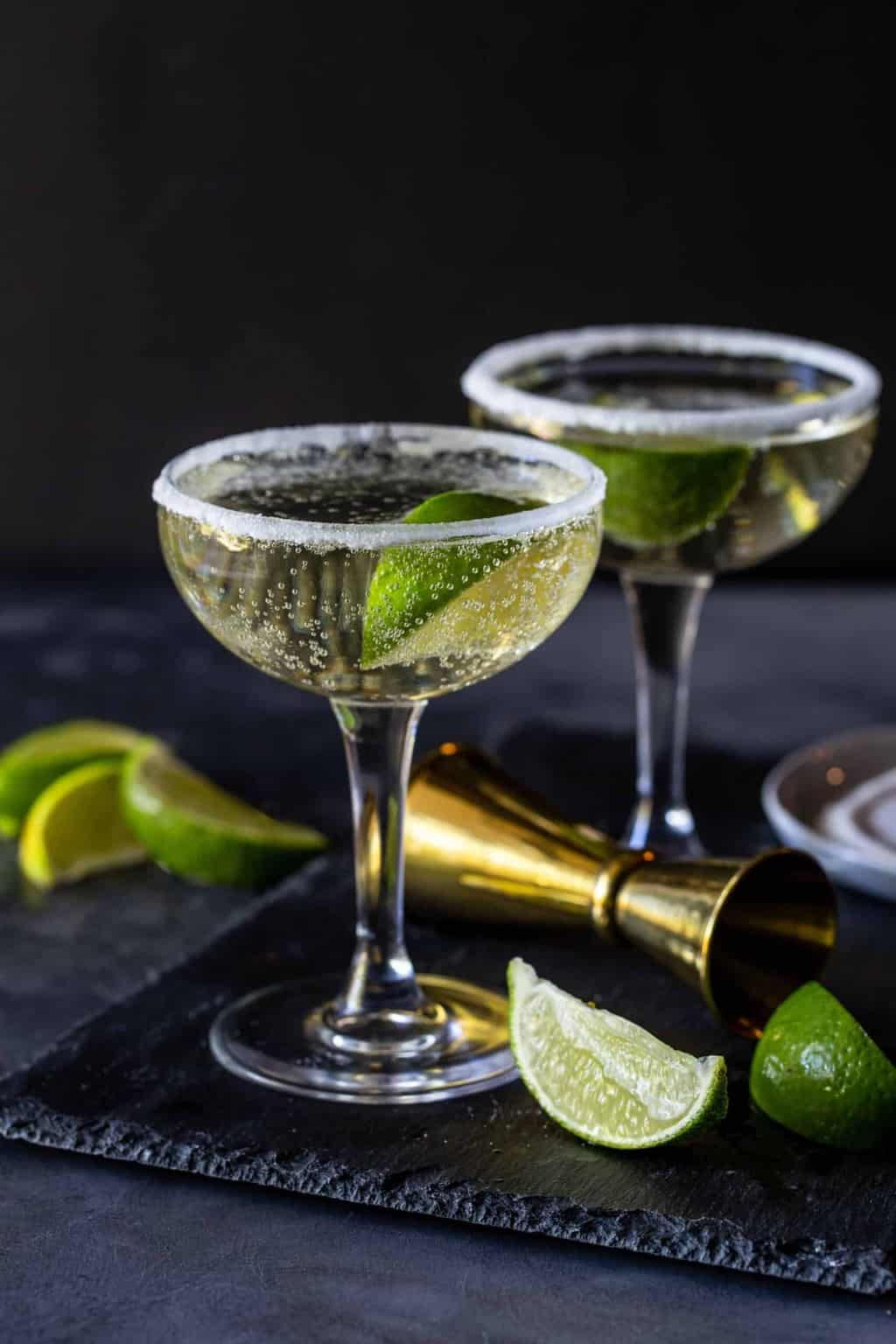 Cocktails in coupe glasses with sugar rims and a lime wedge for garnish.