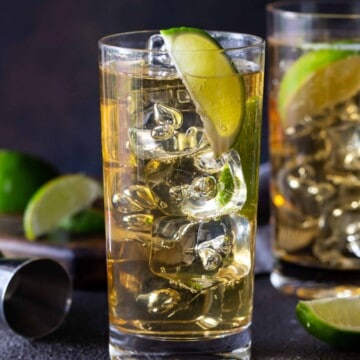 Two highball glasses filled with whiskey and ginger ale, with fresh lime wedges on a dark background.