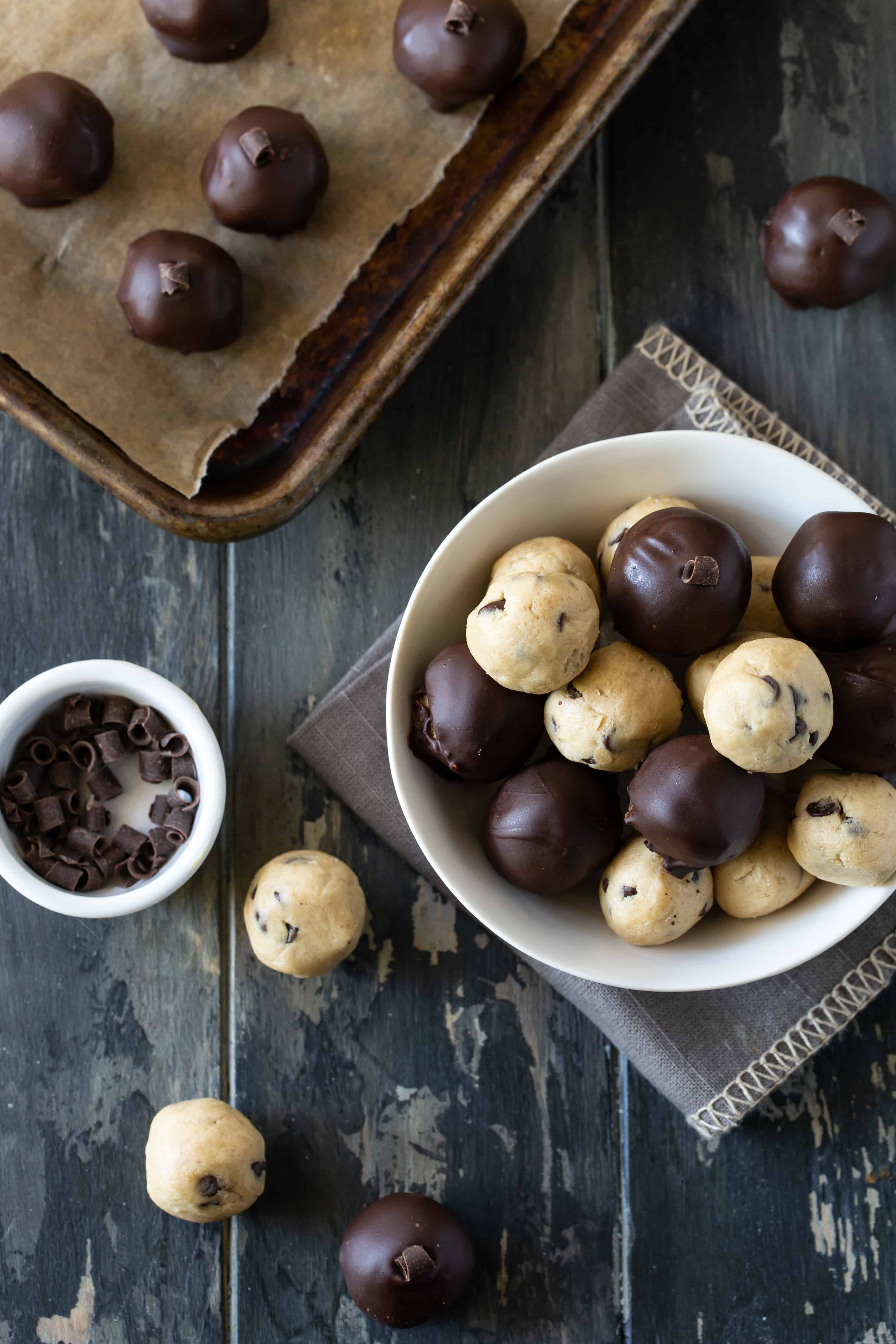 Chocolate dipped truffles in a white bowl and on a sheet pan. Some have been dipped in chocolate.