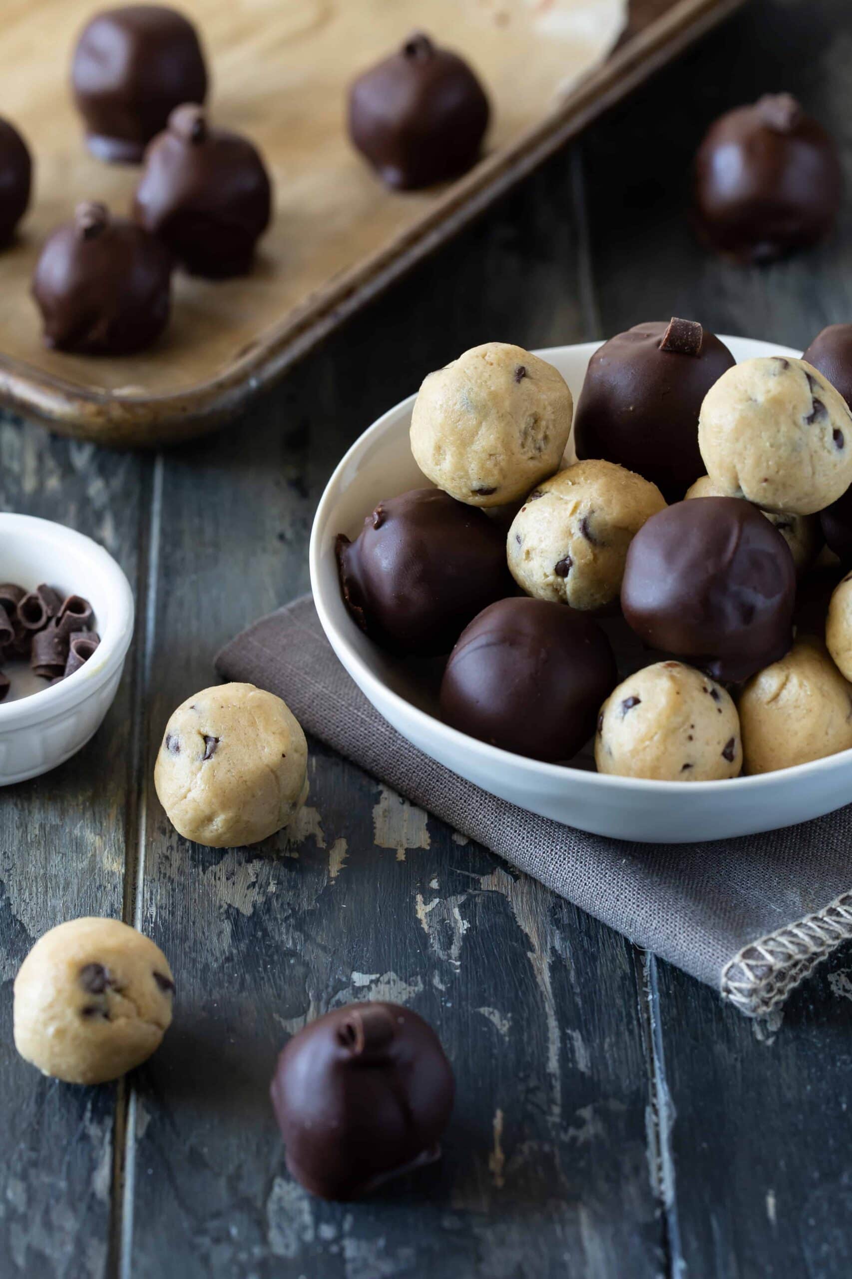 Cookie dough truffles in a white bowl and on a sheet pan. Some dipped in chocolate. 