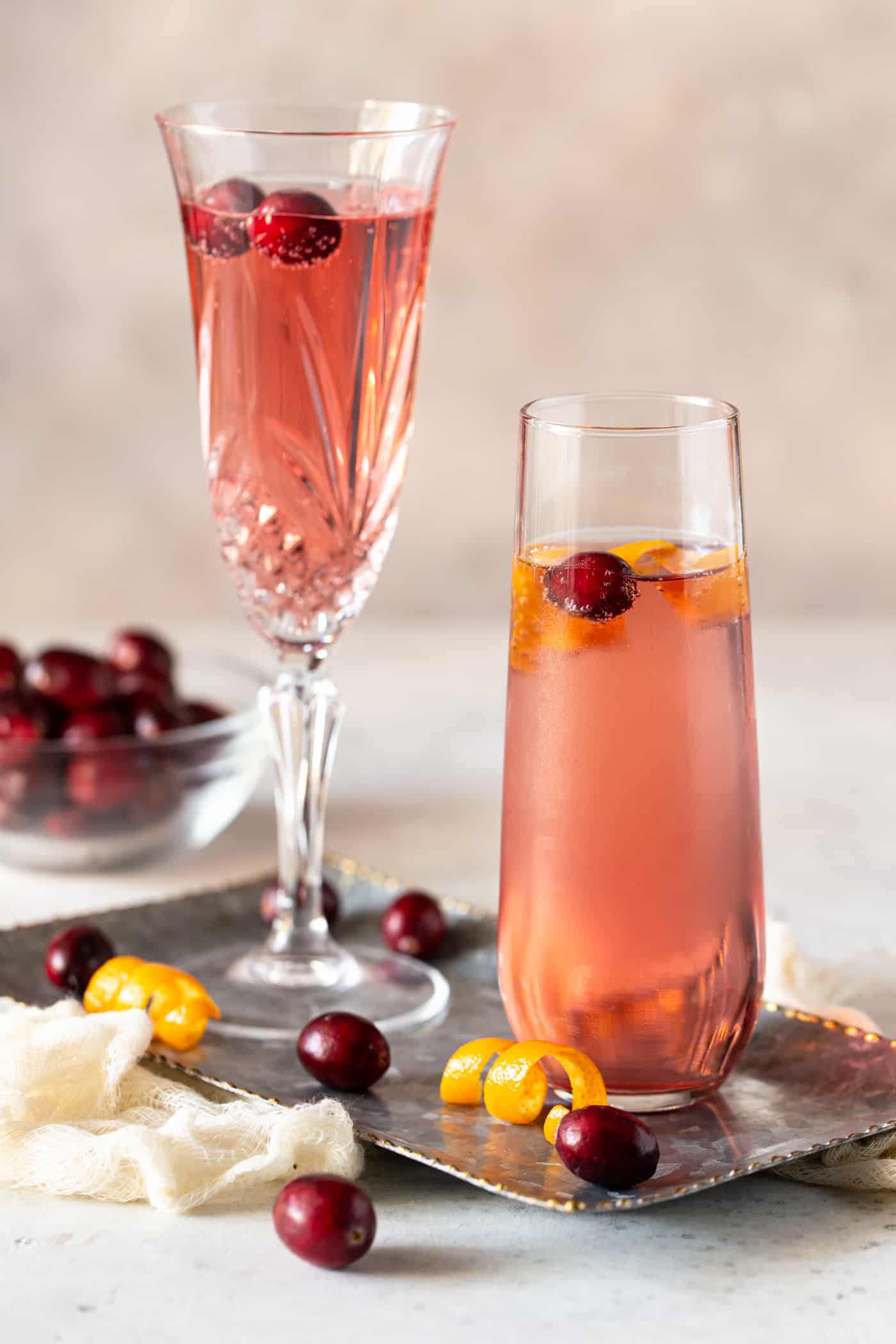  Cocktails in champagne flutes on a silver tray with fresh cranberries for garnish.