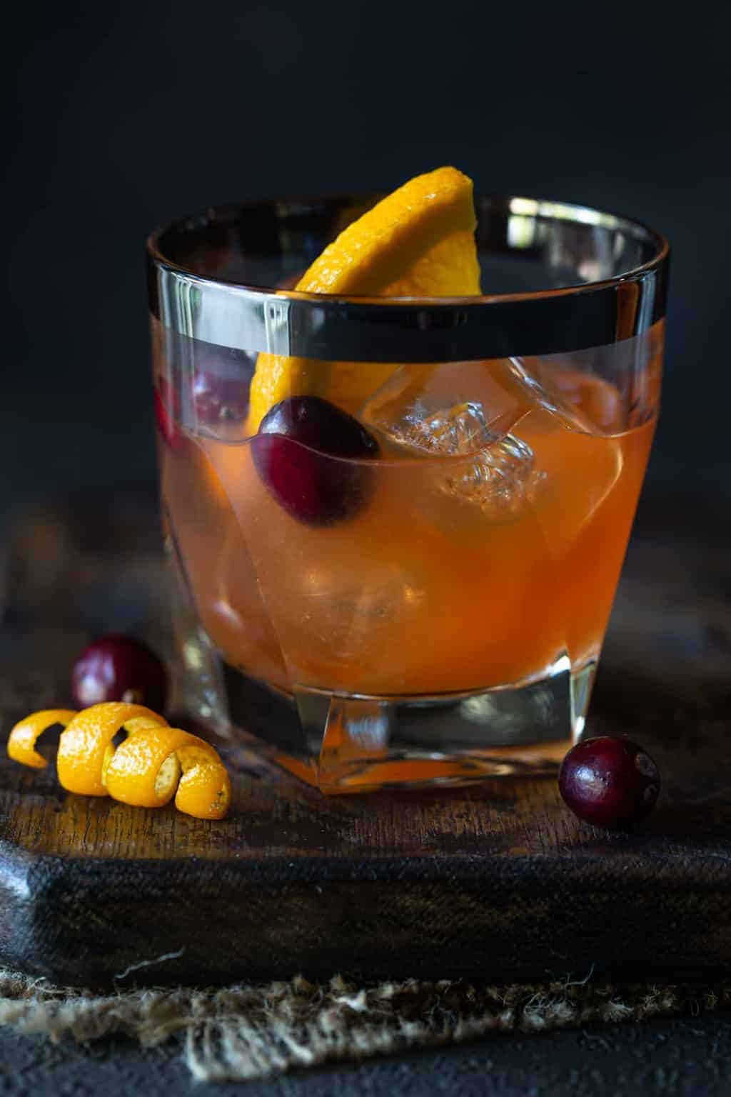 a single lowball glass of Cranberry Whiskey Sour Cocktail. Garnished with fresh cranberries, an orange twist and a fresh orange slice.
