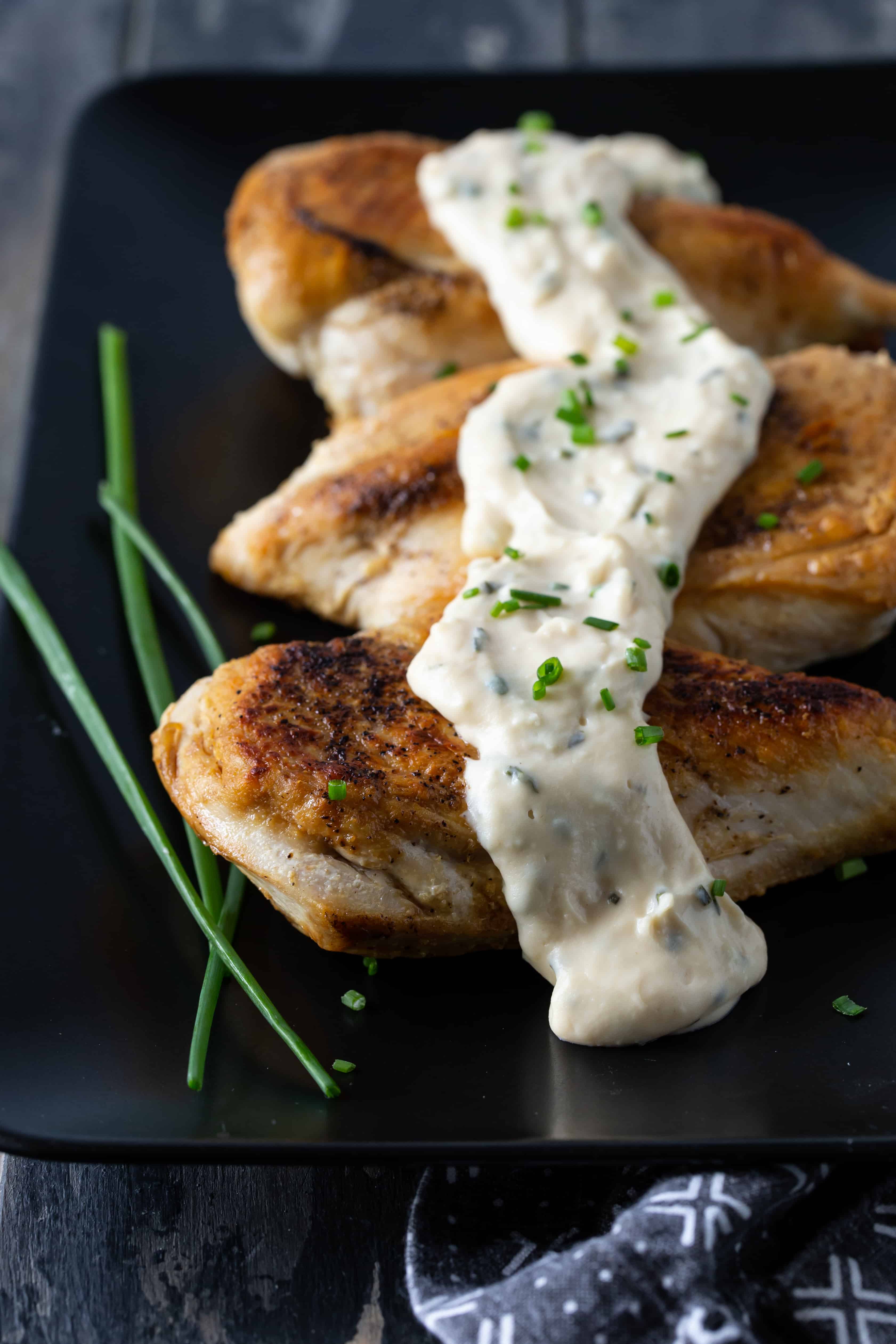 A close up of chicken with feta cheese sauce, with chives.