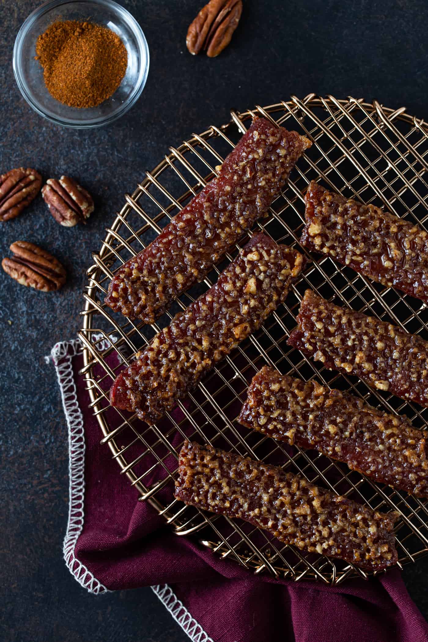 Candied bacon on a rose gold trivet with pecans on the side.