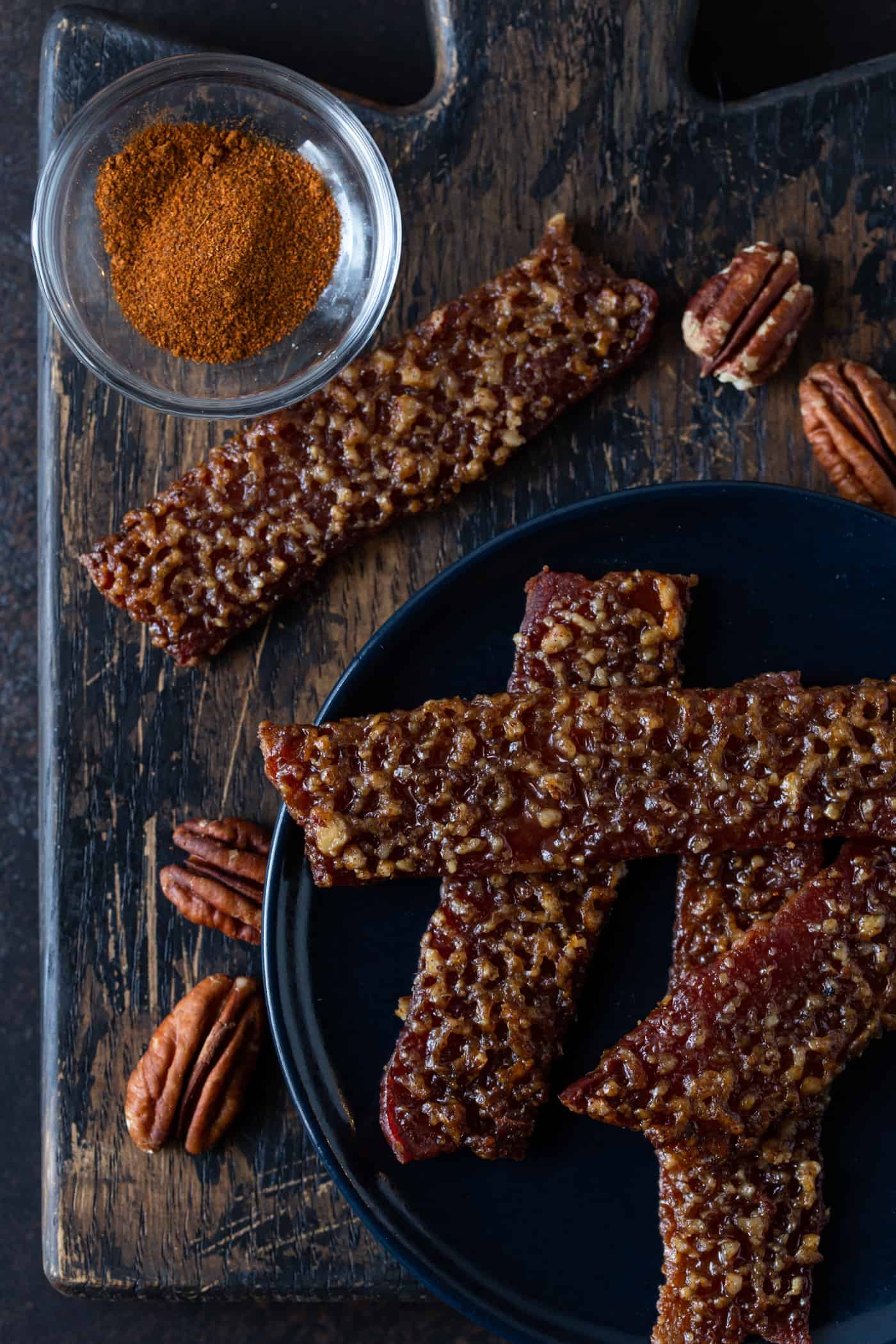 Candied Bacon on a dark plate with cayenne pepper.