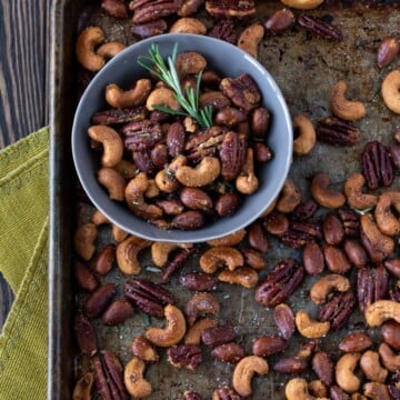 roasted nuts on a baking sheet and in a bowl with rosemary garnish.