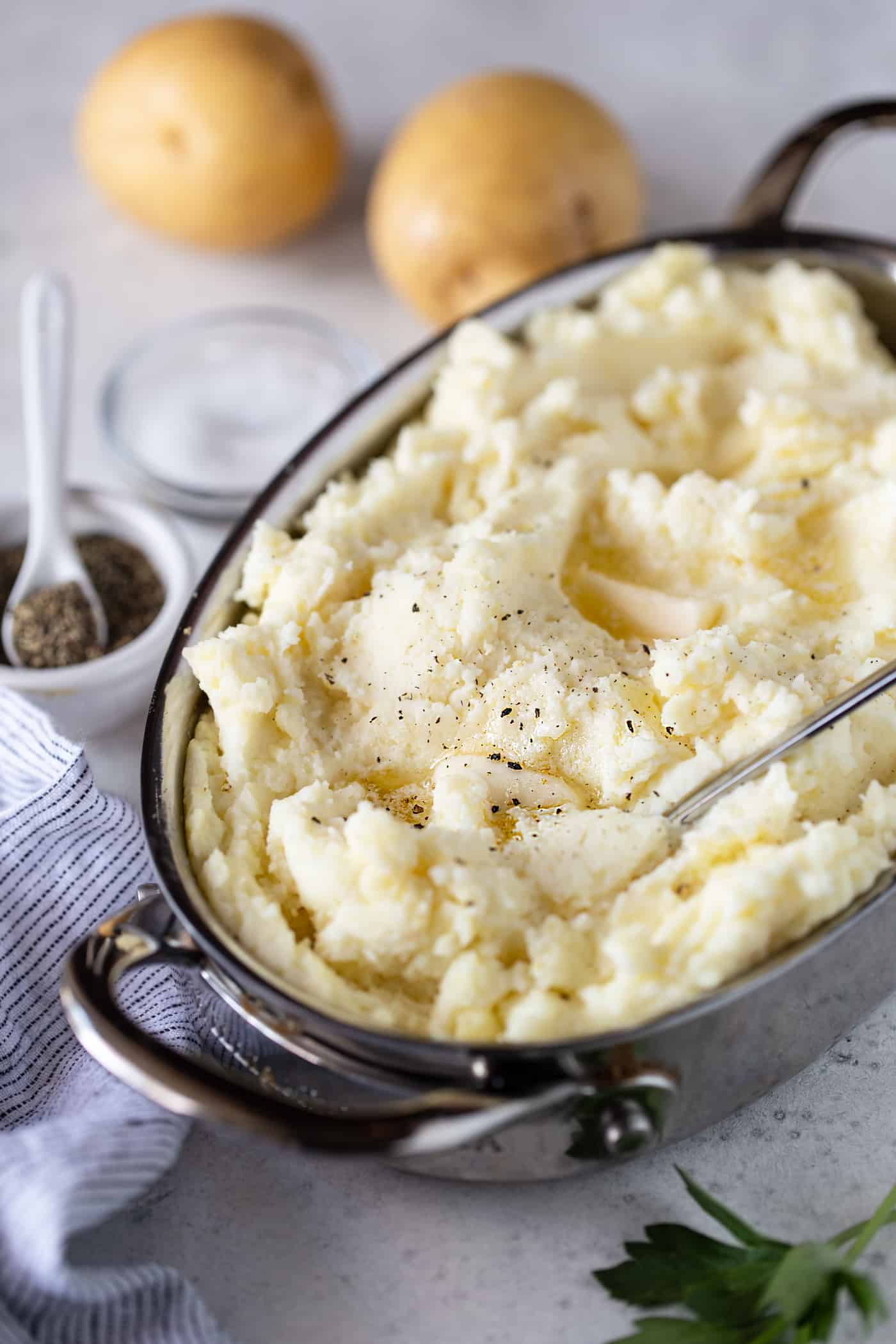Mashed potatoes in a silver baking dish garnished with freshly ground pepper and melted butter.