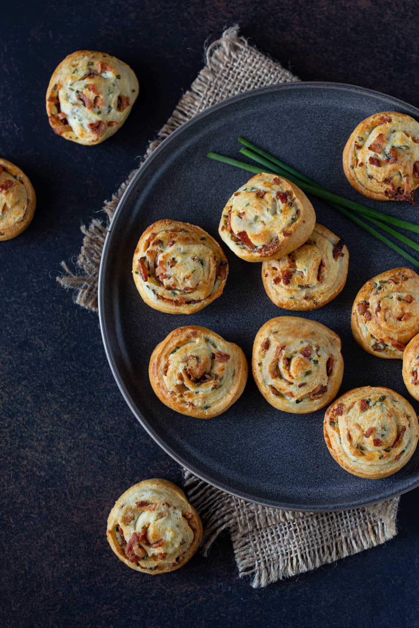 Bacon Cream Cheese Crescent Roll Appetizers on a dark gray plate. Garnished with fresh chives. 