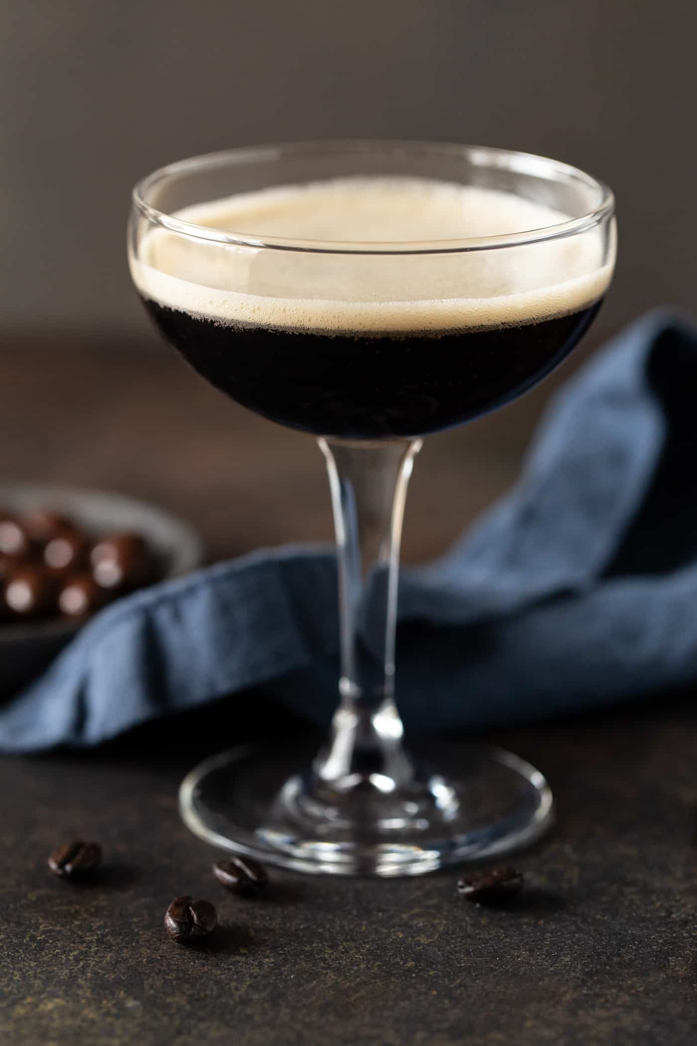 Single Espresso martini with chocolate covered espresso beans and coffee beans for garnish on a dark background.