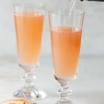 2 champagne flutes filled with mimosa on a white background.