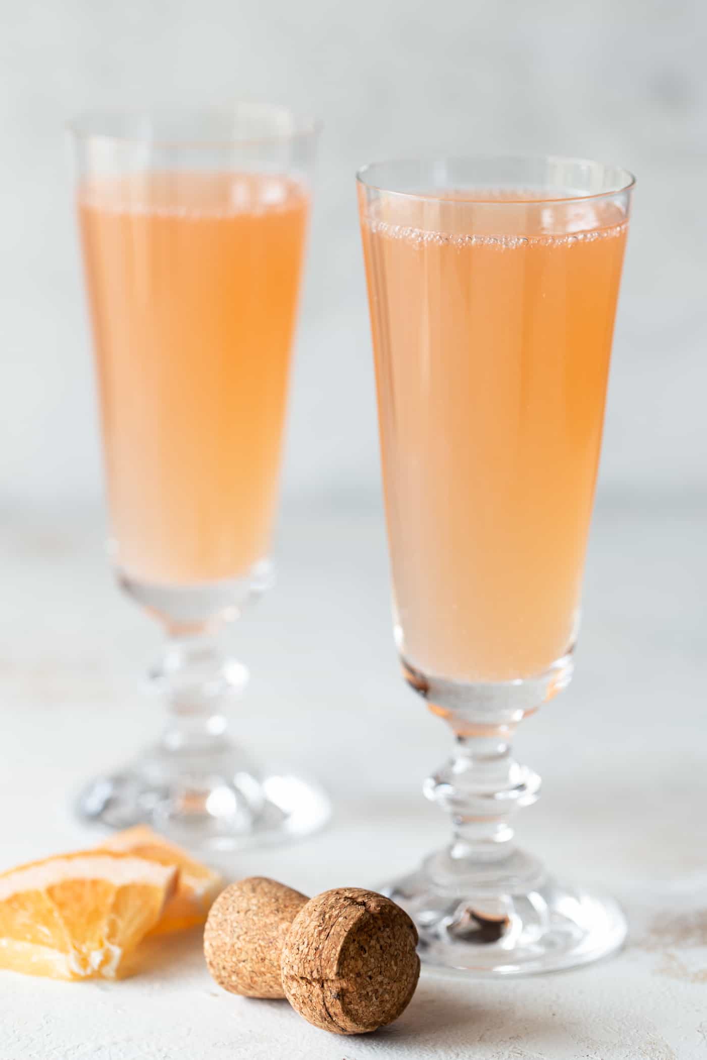 2 mimosas in champagne flutes with fresh grapefruit chunks for garnish.