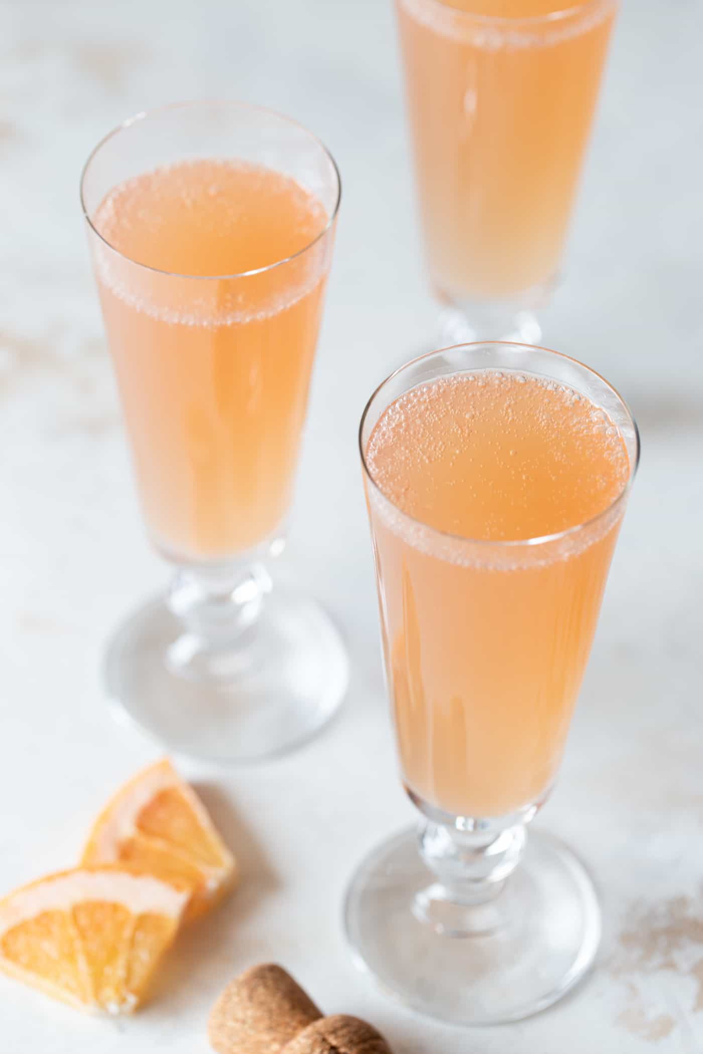 grapefruit mimosas in champagne flutes garnished with fresh grapefruit on a white background.