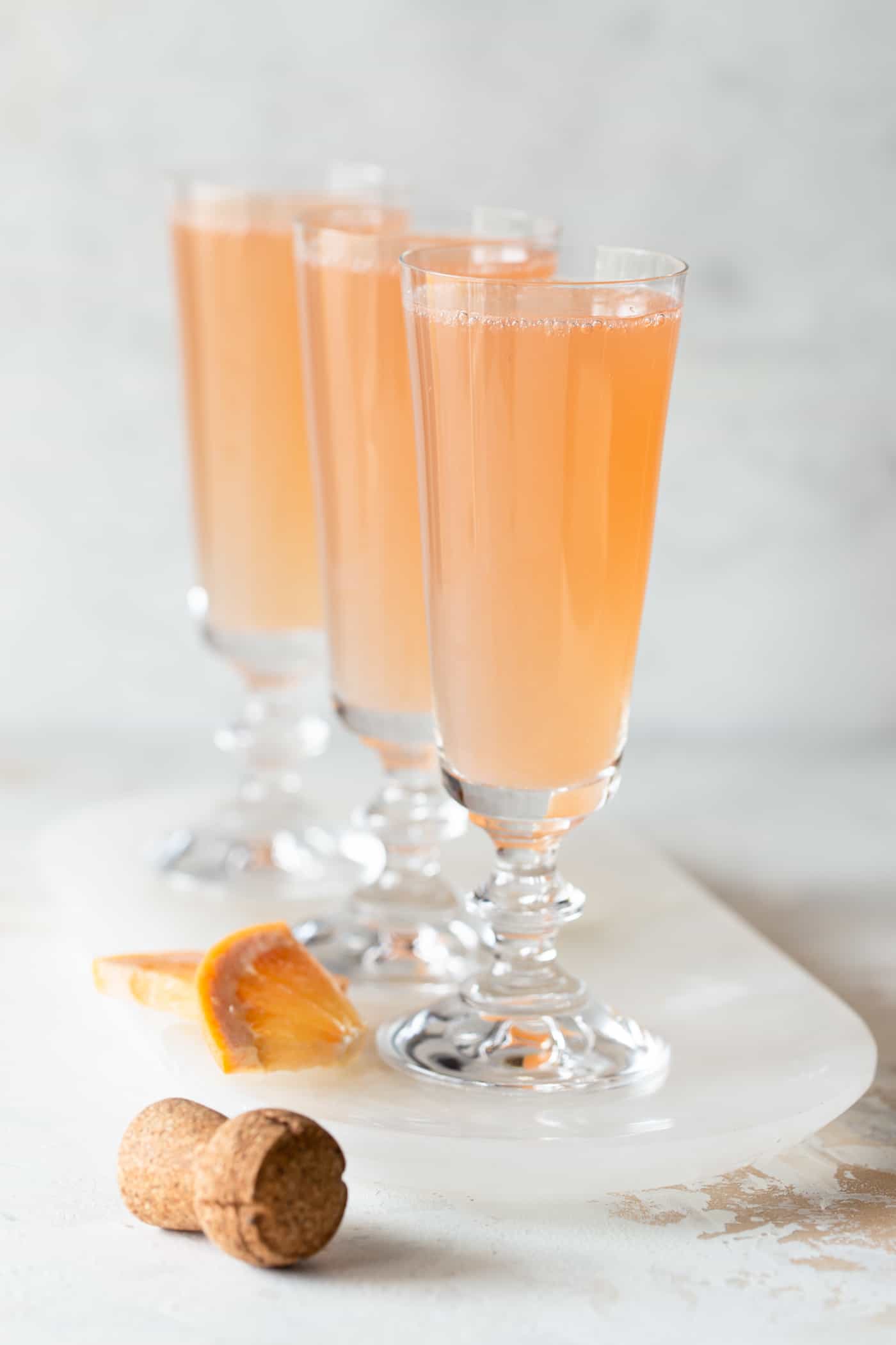  mimosas on a white tray with a white background and fresh grapefruit chunks for garnish.