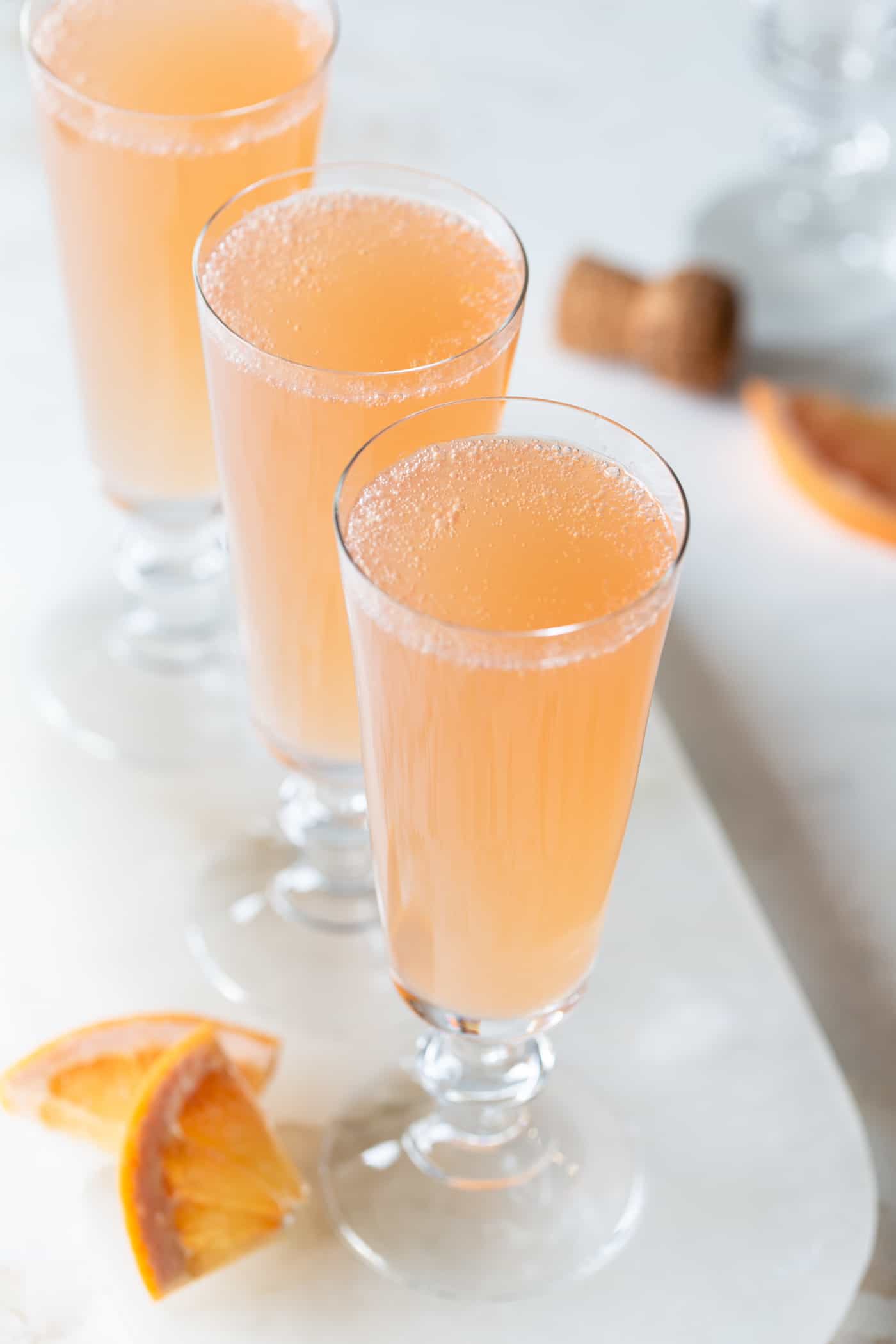 grapefruit mimosas on a white tray with fresh grapefruit wedges,on a white background.