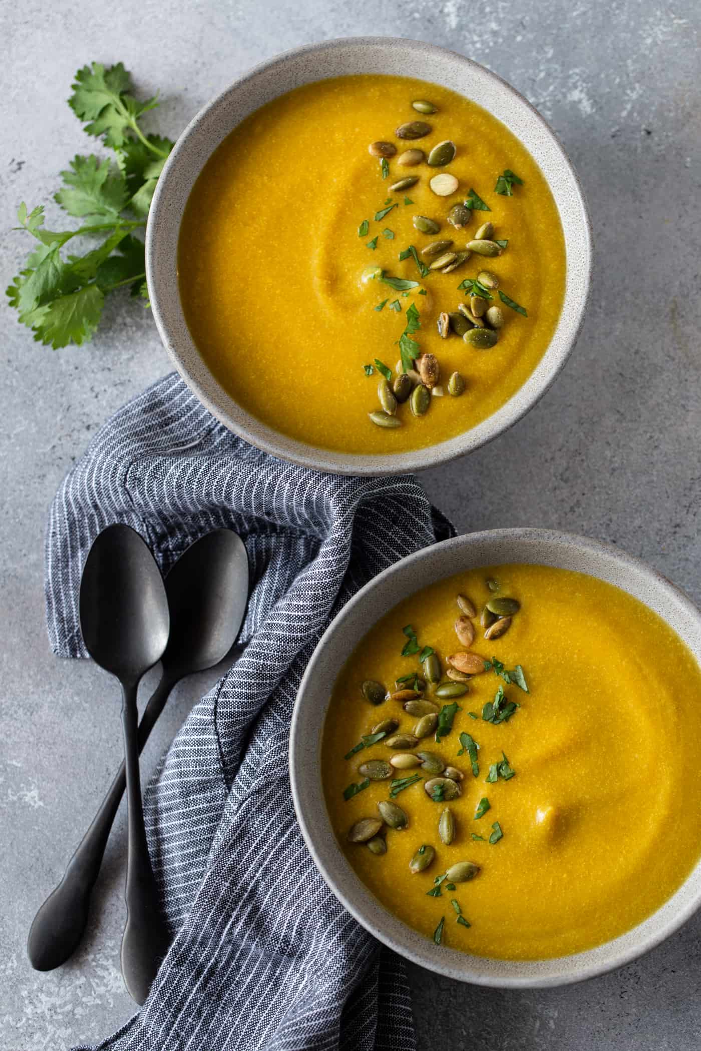 Two bowls of soup garnished with pepitas and fresh cilantro. 