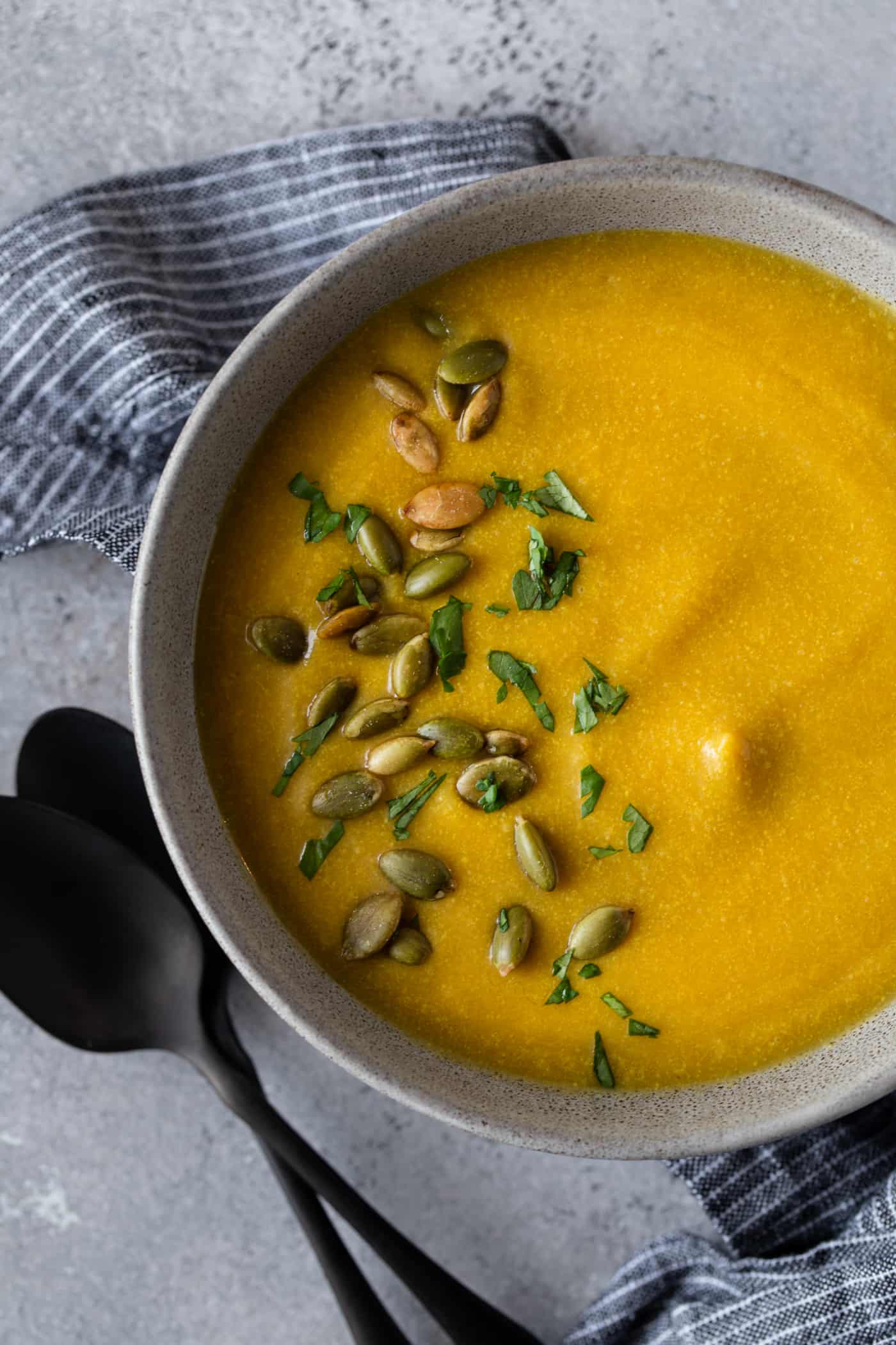 Single gray bowl filled with soup. Garnished with chopped fresh cilantro and roasted pepitas.