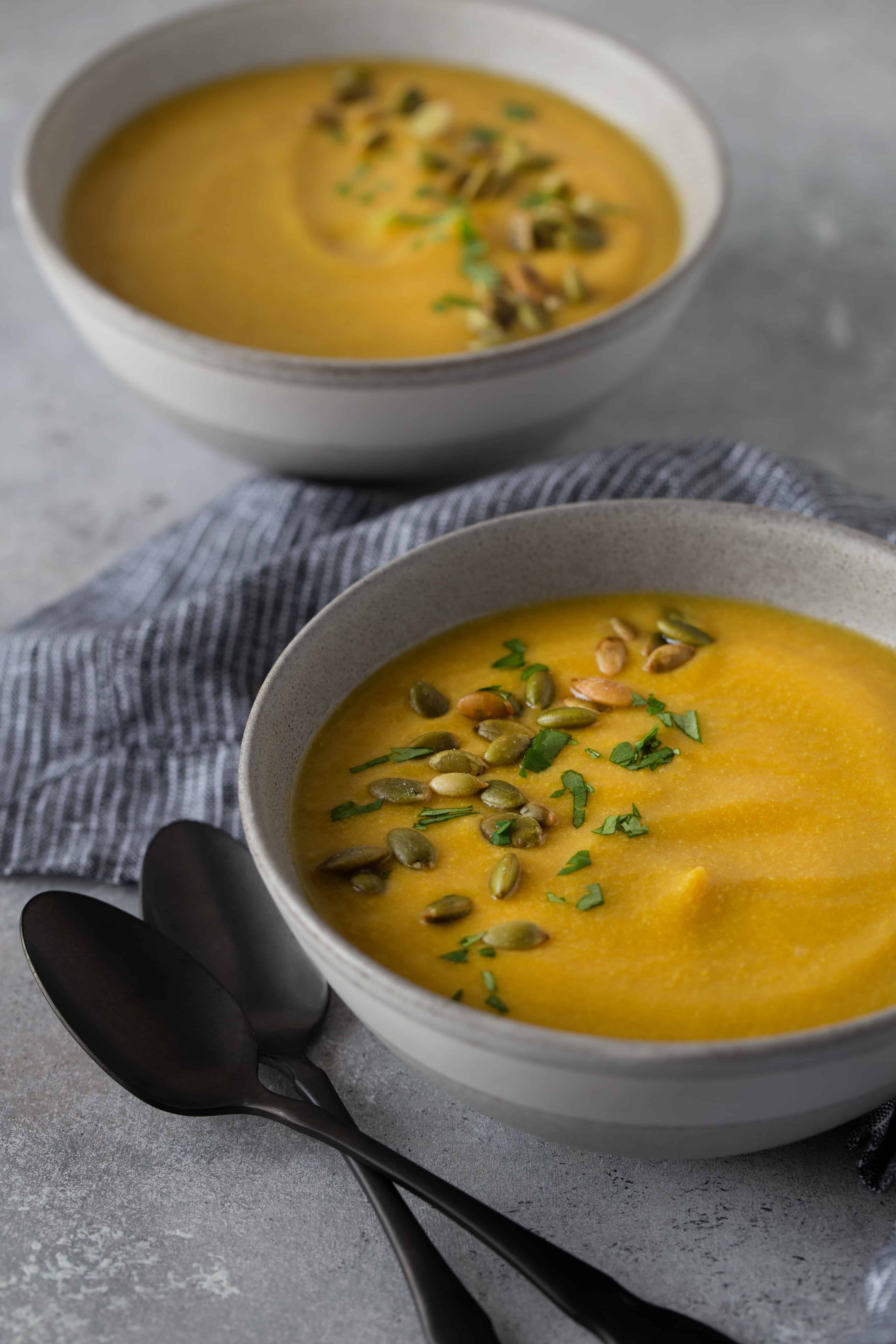 Two bowls filled with soup along with striped napkin and two black spoons. 