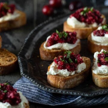 A plate of food with crostini on a table, with Cheese and Cranberry.