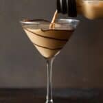 Glass shaker pouring chocolate drink into martini glass swirled with chocolate sauce.