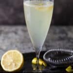 single champagne flute filled with drink and lemon wedge.