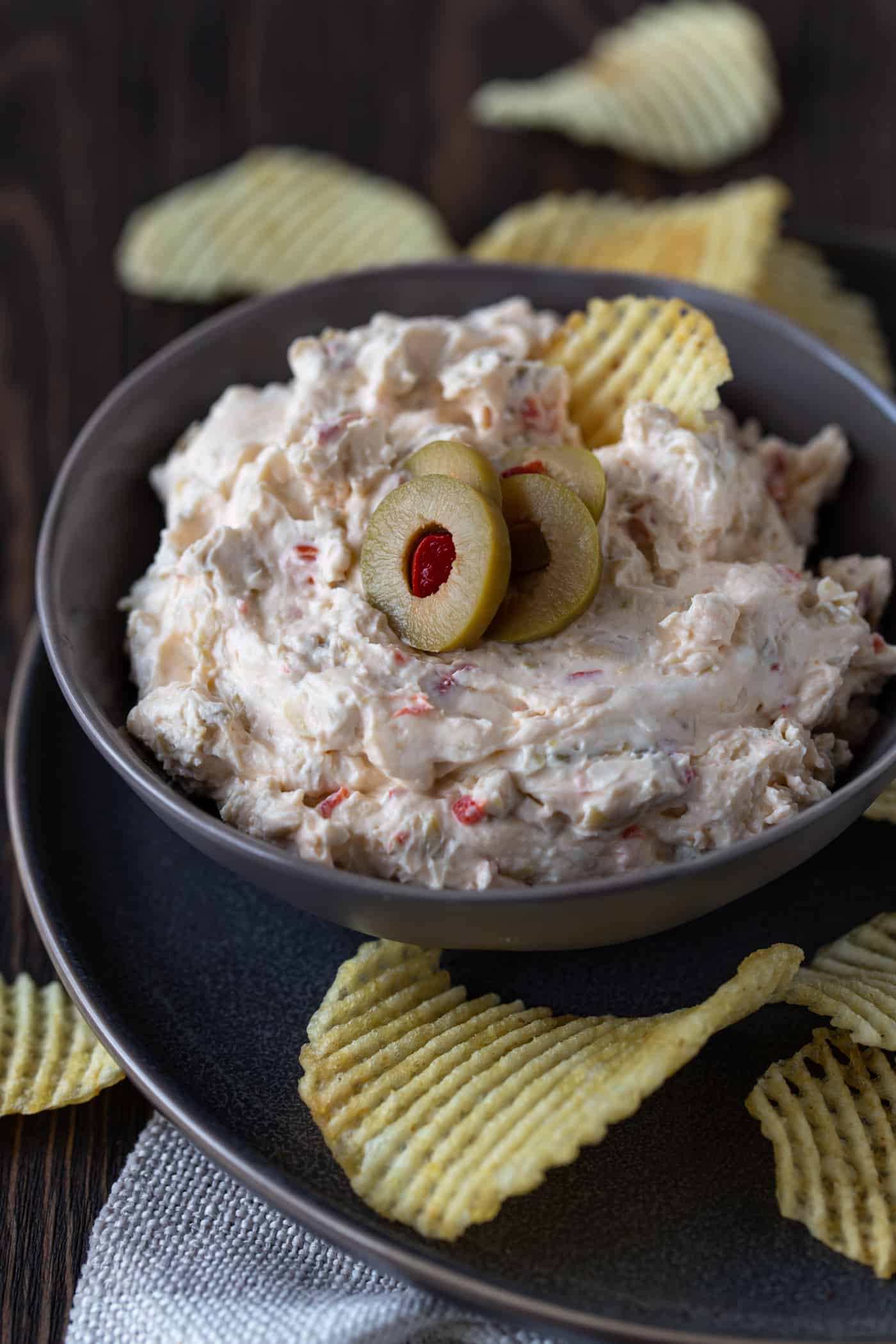 A bowl of green olive dip on a plate with chips.