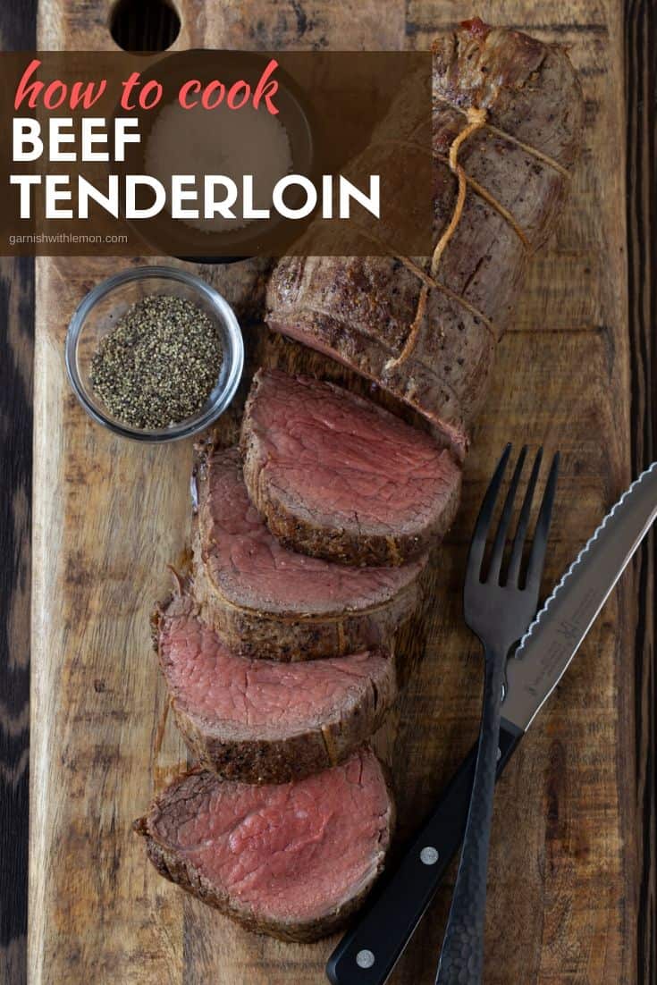 Sliced beef tenderloin on a dark brown cutting board with salt and pepper on side.
