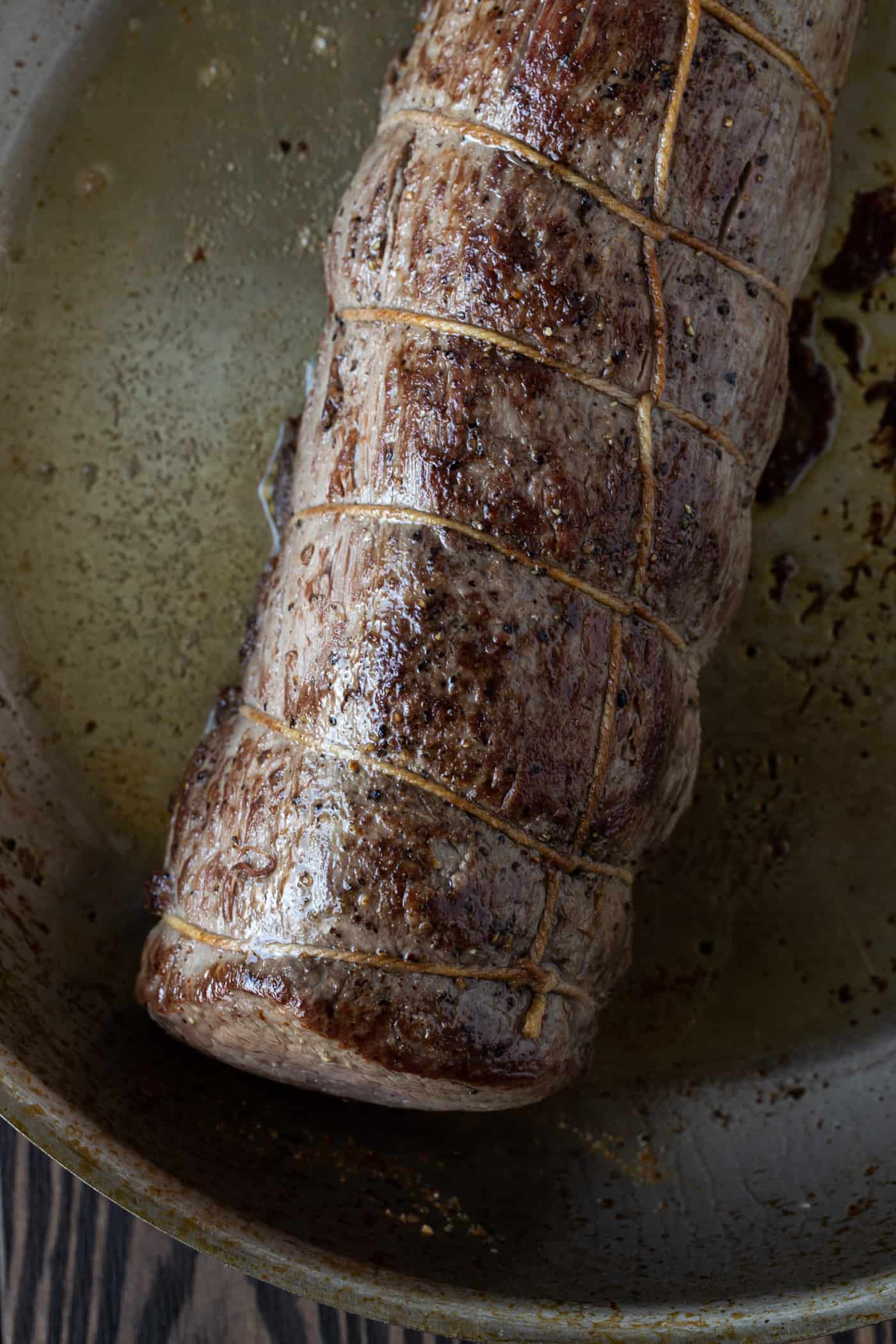 Uncut roasted beef tenderloin in skillet.