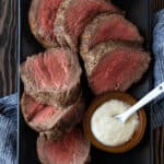 Sliced beef tenderloin on a platter with creamy horseradish for serving.