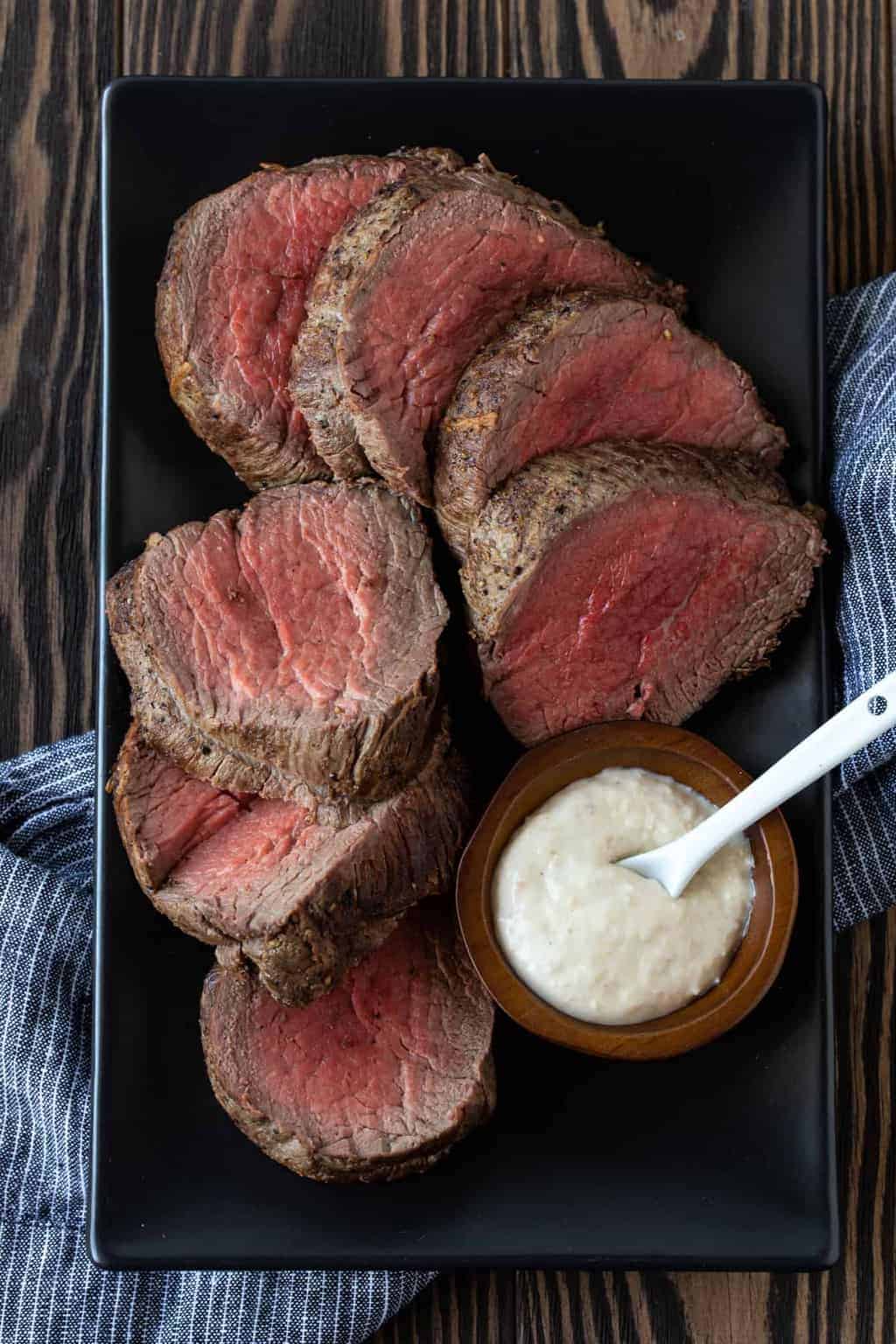 Sliced beef tenderloin on a platter with creamy horseradish for serving.